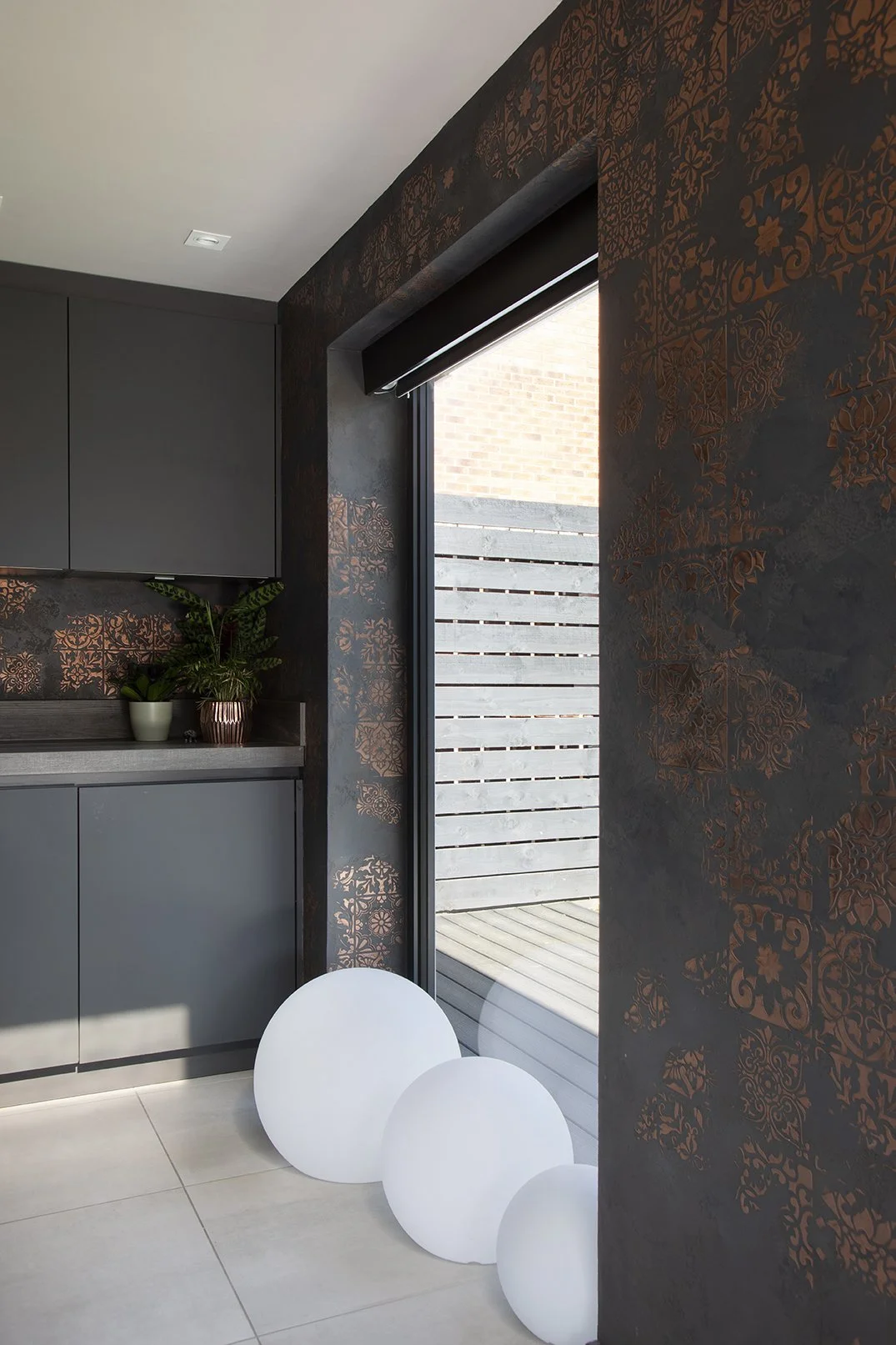 Dark kitchen with bifold doors open to garden, black and copper Venetian plaster feature wall and white globe floor lights, Lytham Road Tynemouth
