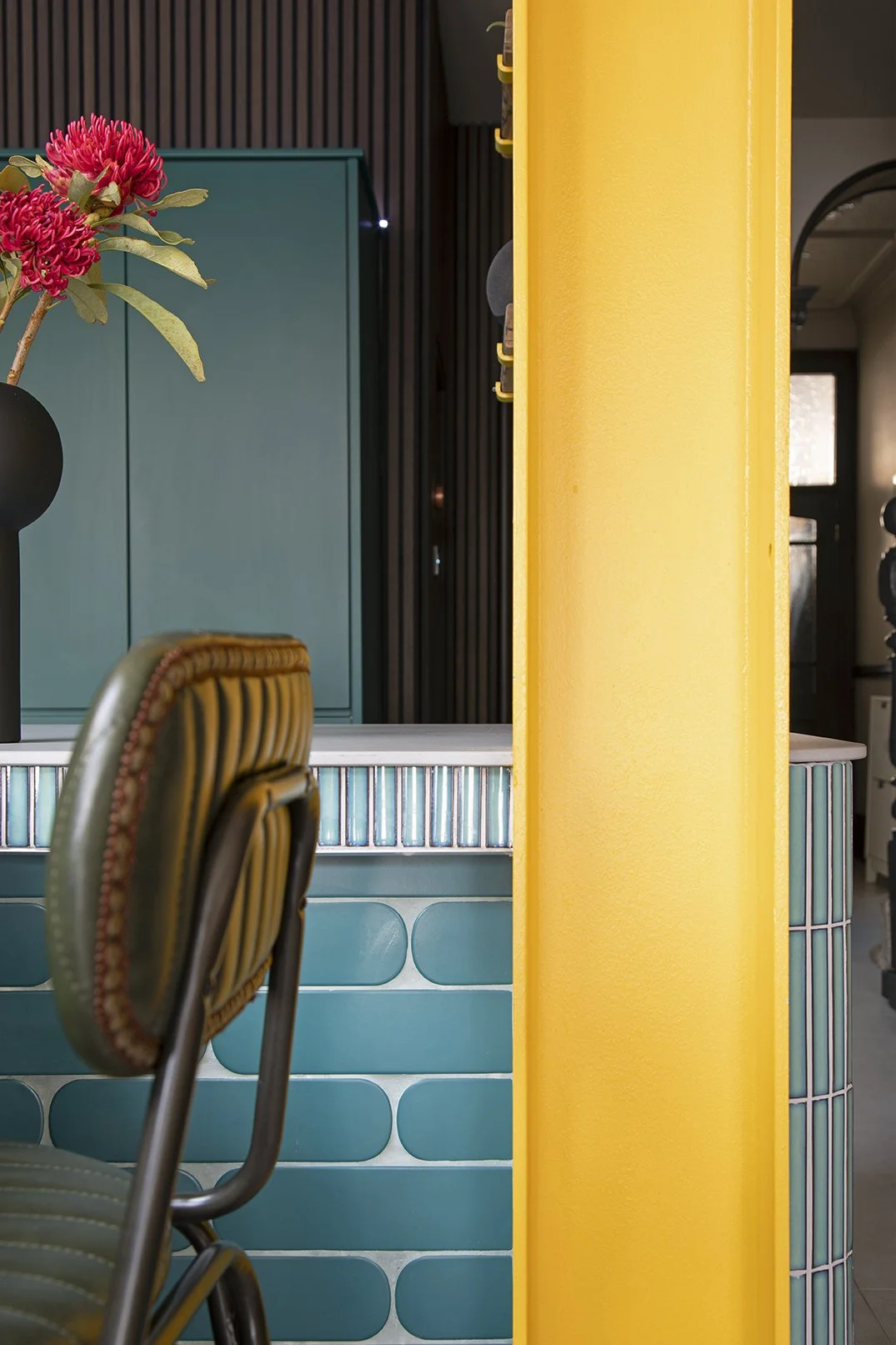 Detail shot of the teal glazed tile kitchen island seating area in a North Shields family home designed by Carole Crowe Interior Design, showing an olive green leather studded bar stool against the tiled island face with a mix of vertical finger tile