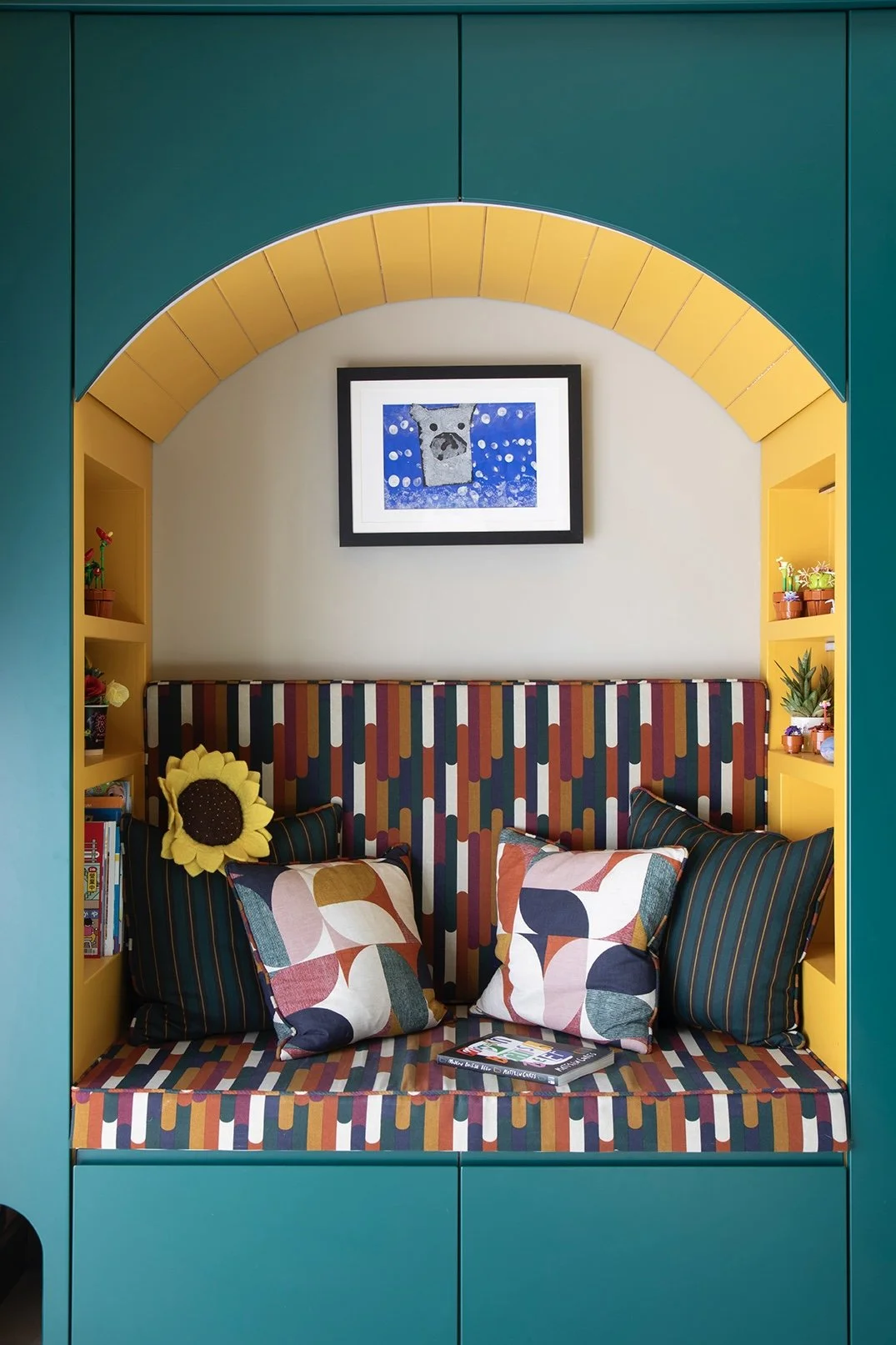 Built-in reading nook set within a yellow tiled arch in the kitchen of a North Shields family home designed by Carole Crowe Interior Design, featuring a banquette seat and backrest upholstered in a bold multicoloured geometric stripe fabric, mixed sc