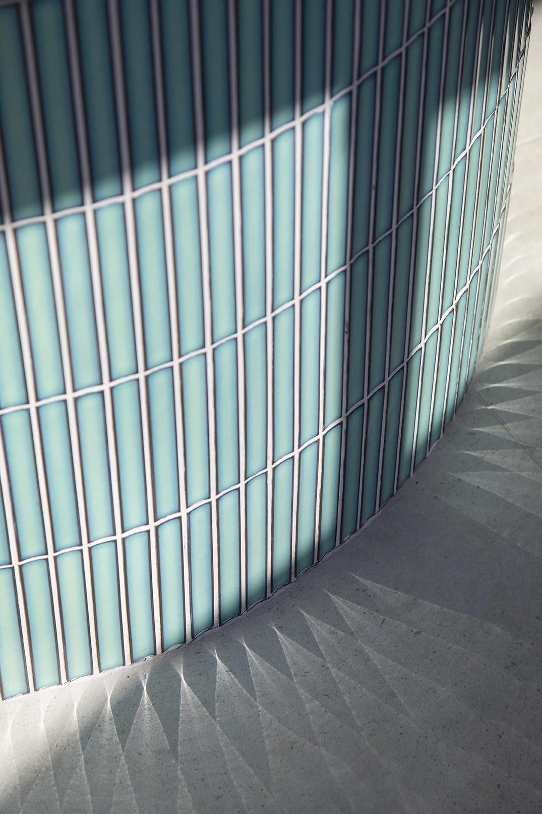 Abstract close-up detail of the curved teal glazed finger tile cladding on the kitchen island in a North Shields family home designed by Carole Crowe Interior Design, showing the varying tones of teal and pale aqua across the handmade glazed tiles wi