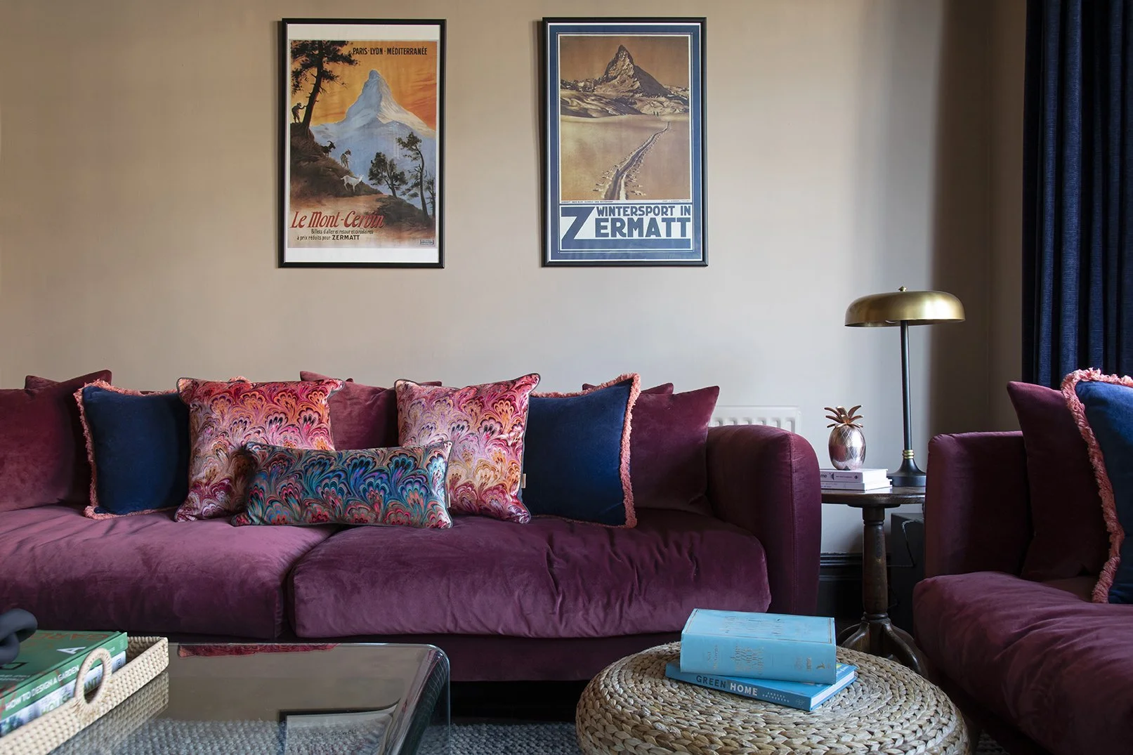 Sitting room in the Queens Road project by Carole Crowe Interior Design, Whitley Bay, showing a large plum velvet sofa generously styled with navy velvet, coral-fringed plum velvet and multicoloured marbled print cushions, two framed vintage Alpine t