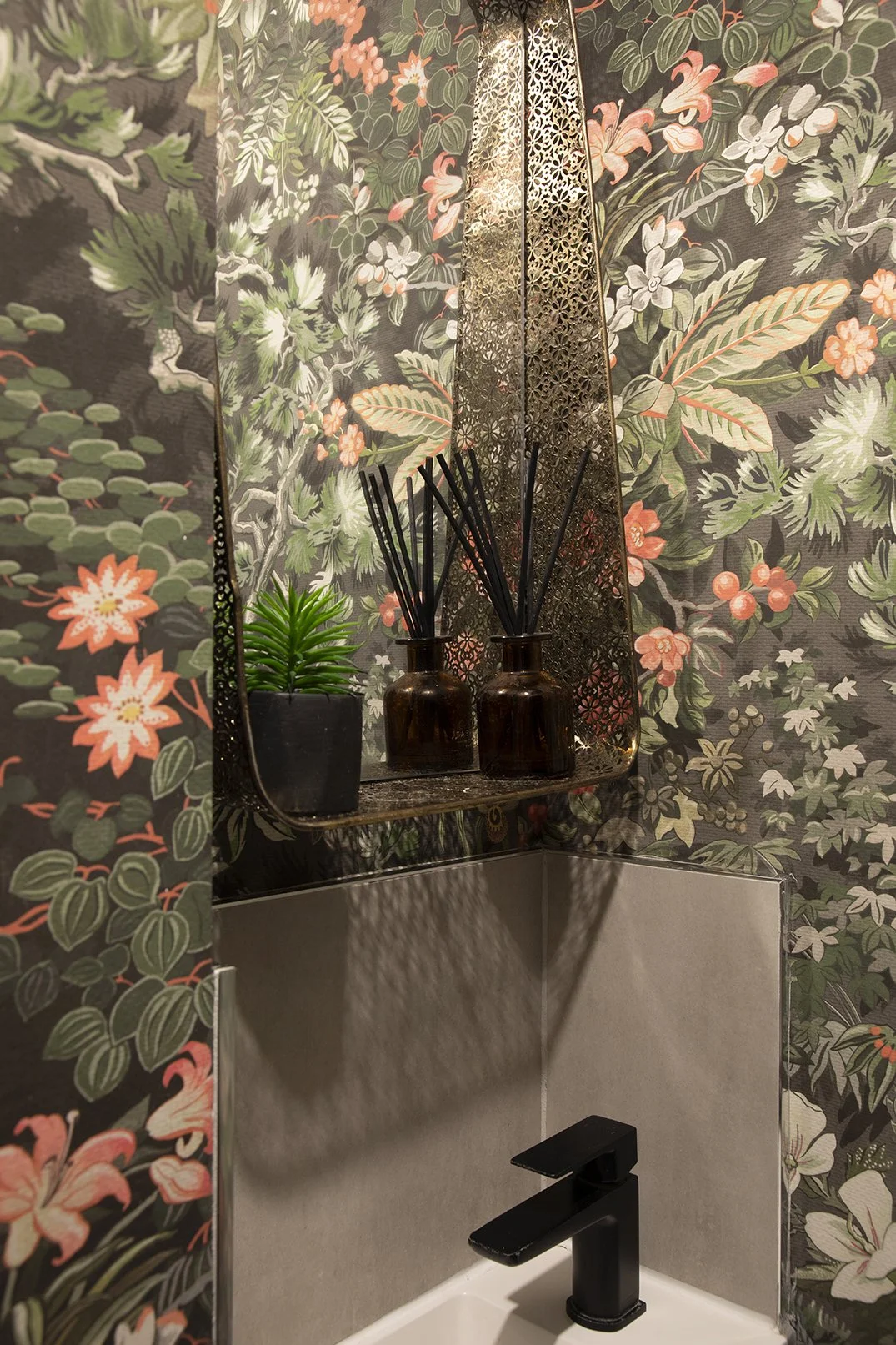 Detail of downstairs cloakroom with dark botanical wallpaper, ornate brass mirror, reed diffusers and black basin tap, Tynemouth