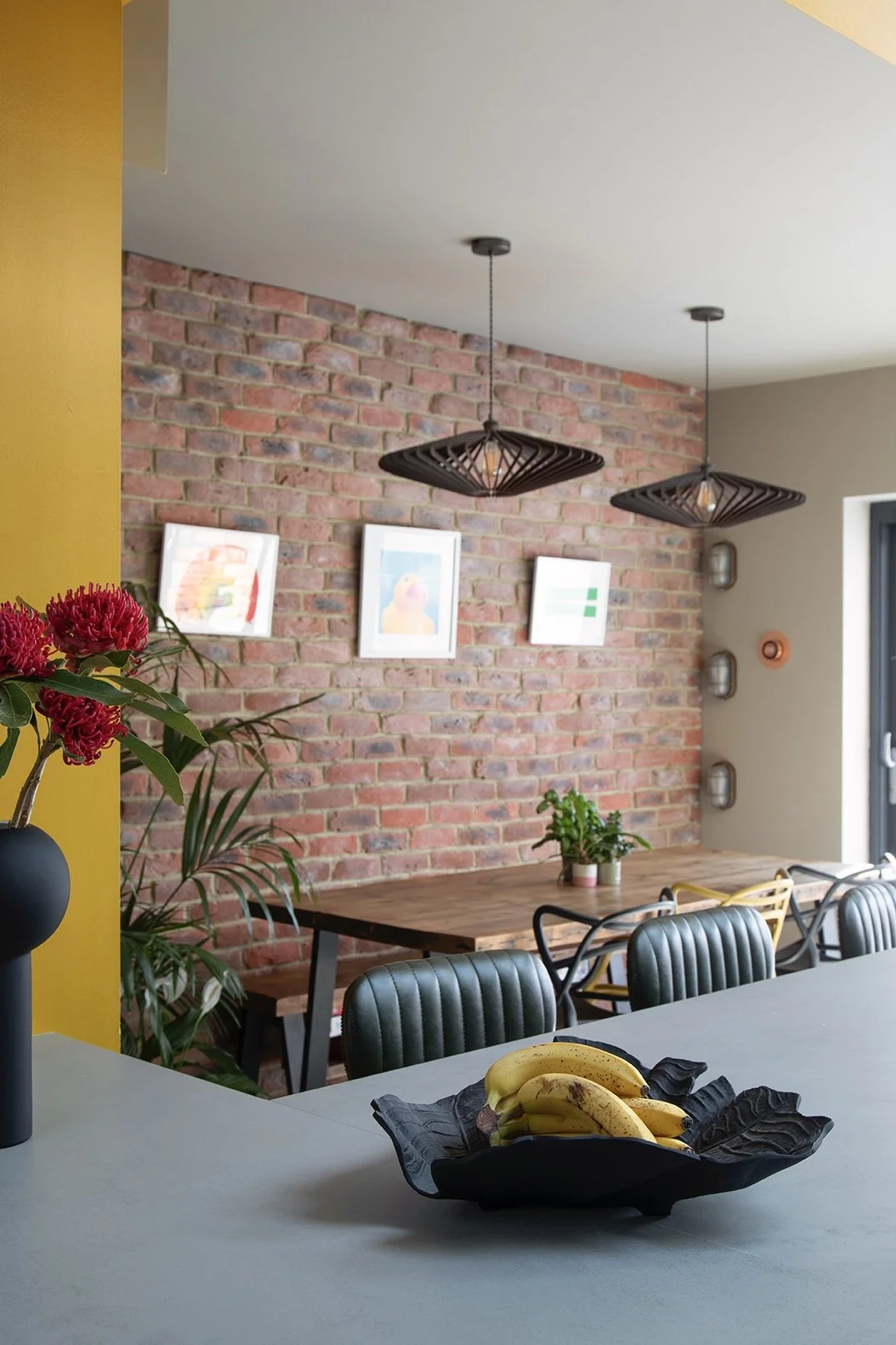 Dining area in a North Shields family home designed by Carole Crowe Interior Design, featuring a solid wood dining table with dark green channel-back leather dining chairs and yellow Masters-style chairs, two large black sculptural pendant lights han