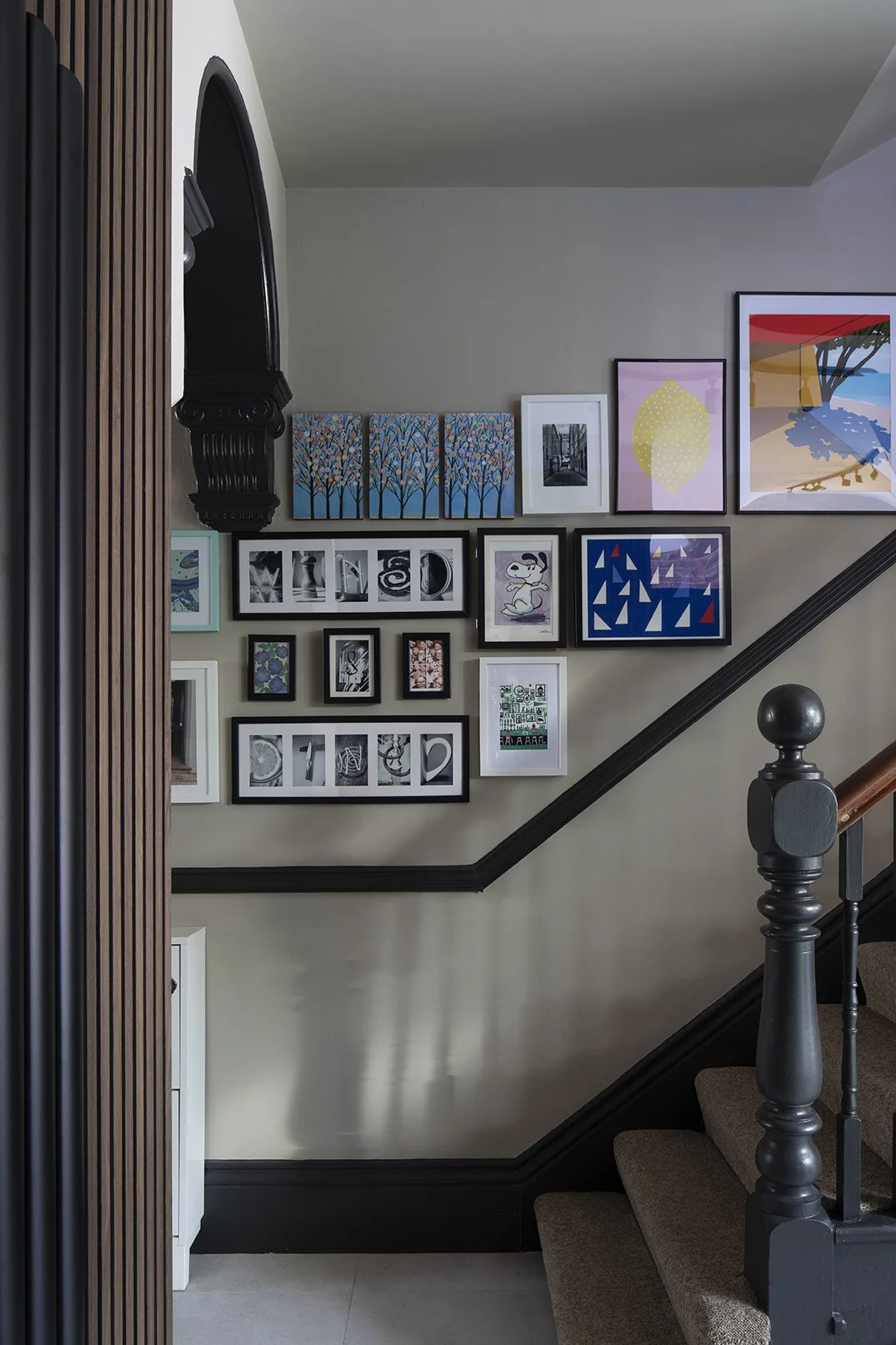 Gallery wall lining the staircase of a North Shields family home designed by Carole Crowe Interior Design, featuring a densely curated mix of framed prints, original paintings and children's artworks in varied sizes and styles including bold colour p