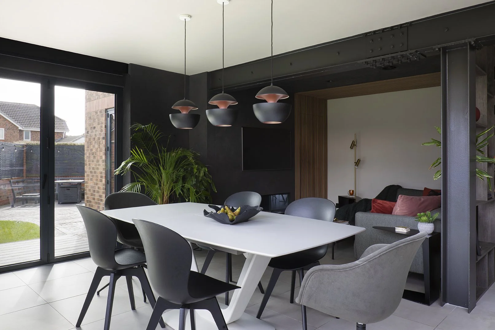 Open-plan dining area with white table, black dining chairs, copper pendant lights and concealed snug opening, Lytham Road Whitley Bay