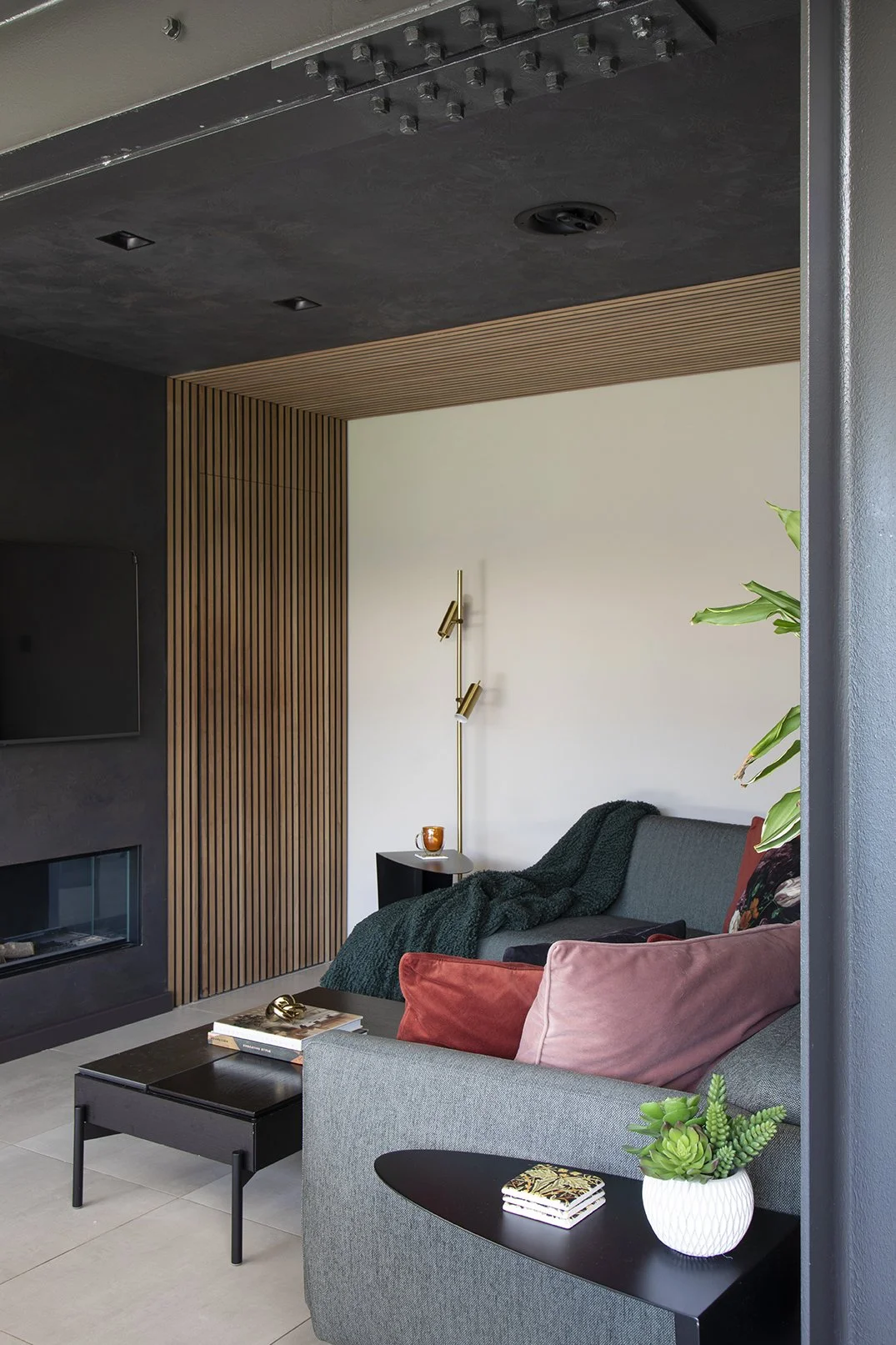 View into concealed snug through oak wood slat framed opening with fireplace, grey sofa and brass floor lamp, Lytham Road Tynemouth