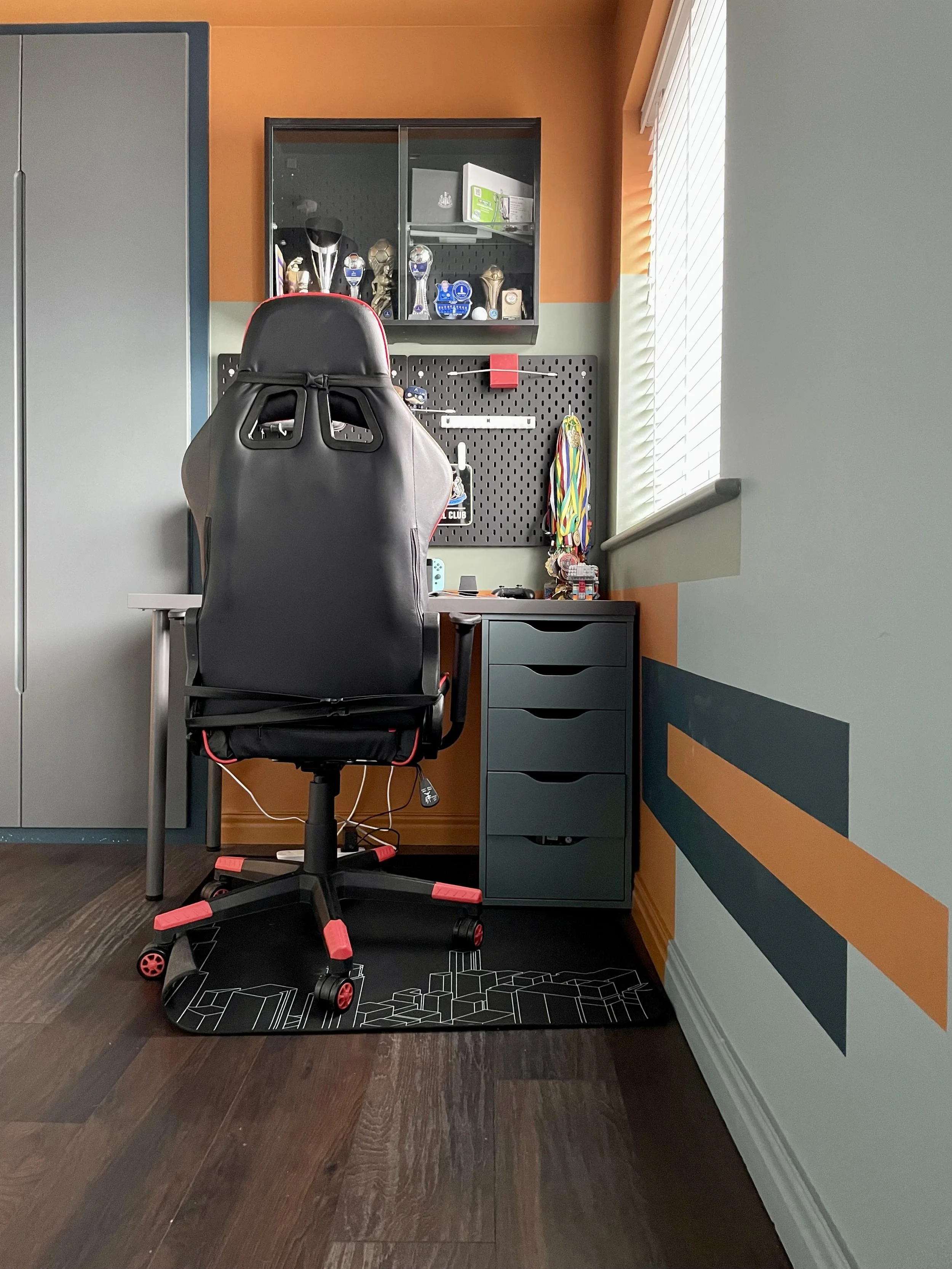 Boys' bedroom gaming corner with orange colour-blocked walls, black racing gaming chair and pegboard desk organiser