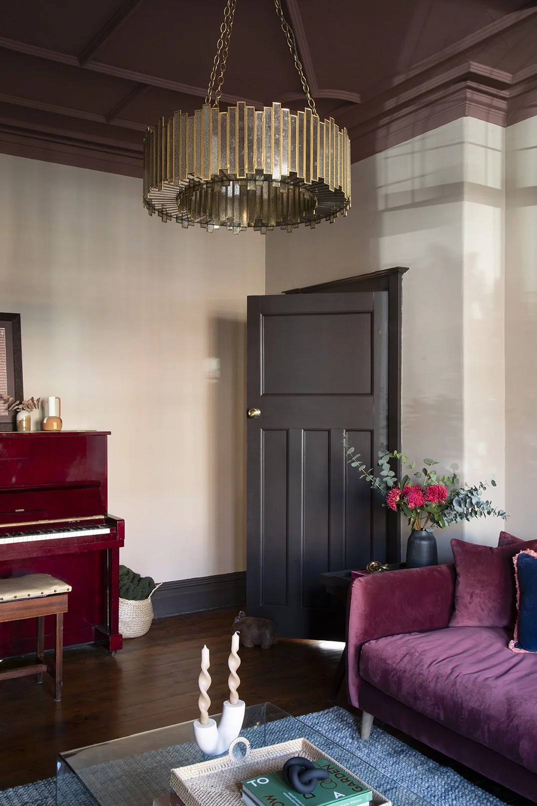 Detail of the sitting room in the Queens Road project by Carole Crowe Interior Design, Whitley Bay, showing the brass and smoked glass drum chandelier hanging from a plum painted ornate plasterwork ceiling, a dark painted Victorian panelled door, a g