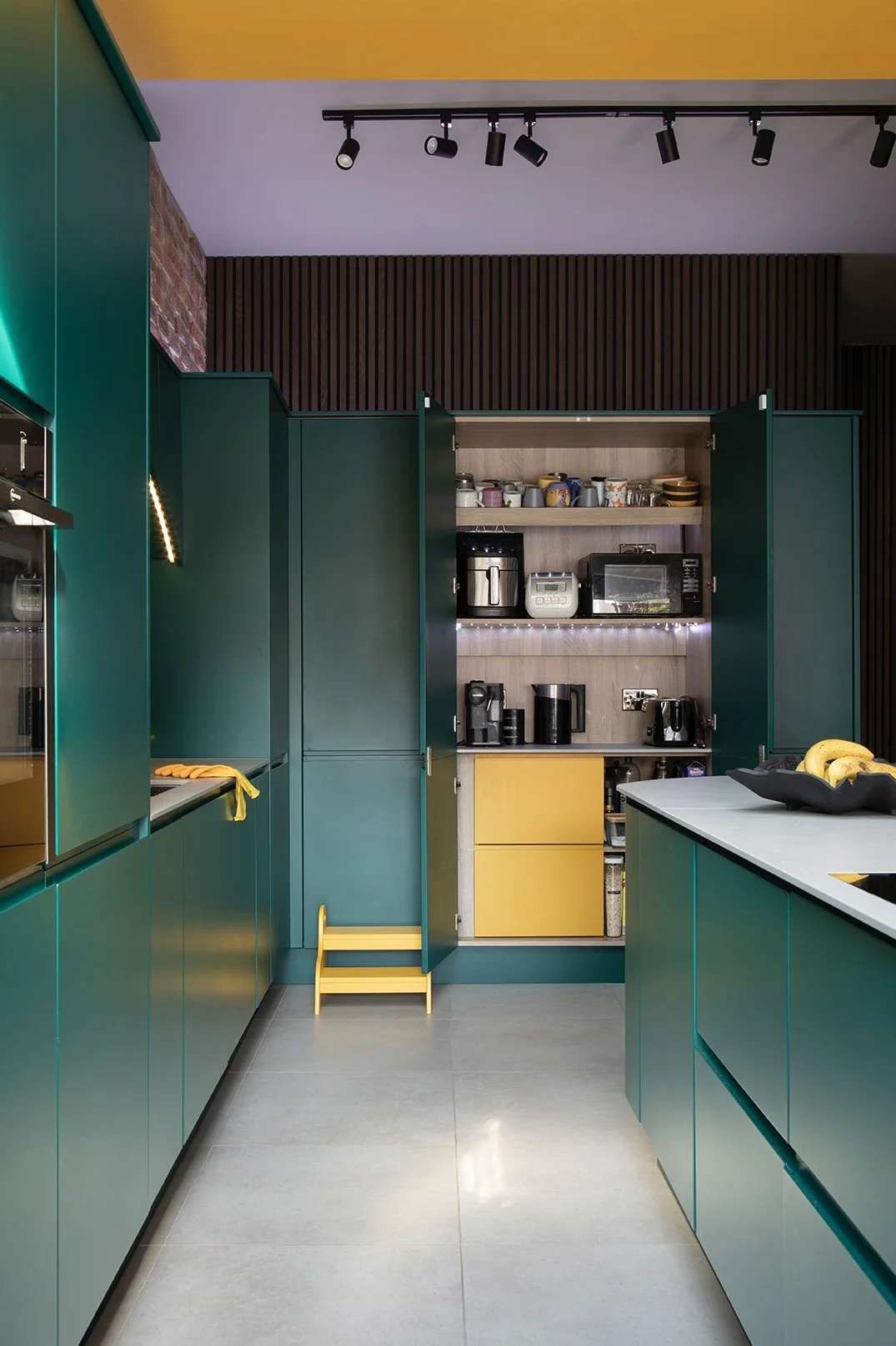 Open concealed appliance cupboard in the kitchen of a North Shields family home by Carole Crowe Interior Design, revealing a fully fitted breakfast station with yellow painted interior cabinetry, integrated shelving for small appliances including a c