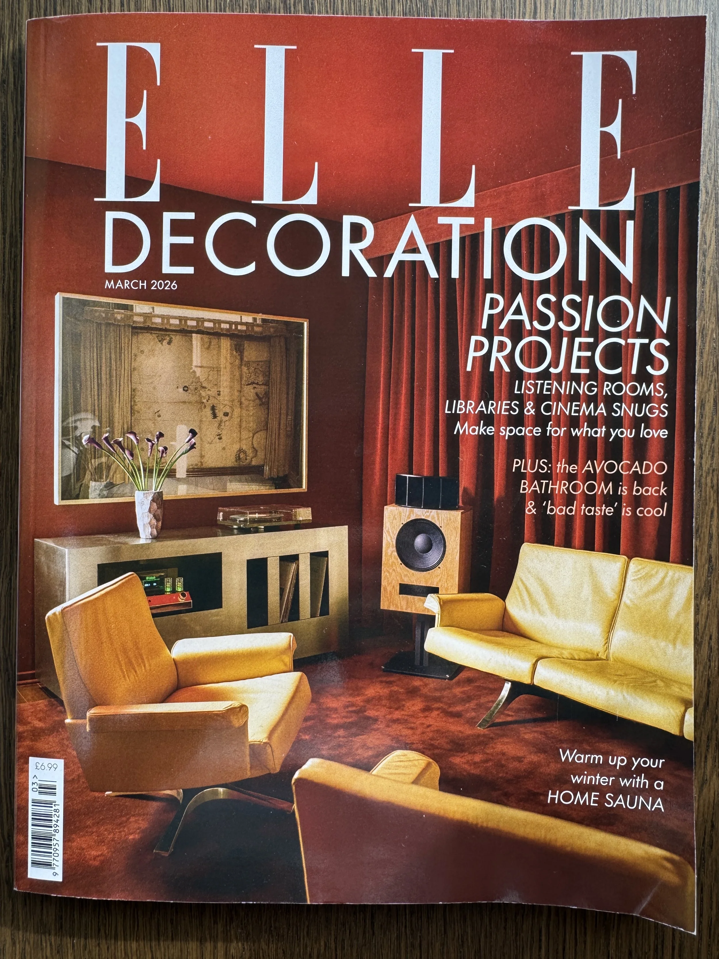 Cover of Elle Decoration magazine, March 2026 issue, featuring a mid-century modern living room with yellow armchairs, a yellow sofa, a wooden speaker, a black and beige console, and red walls with curtains.