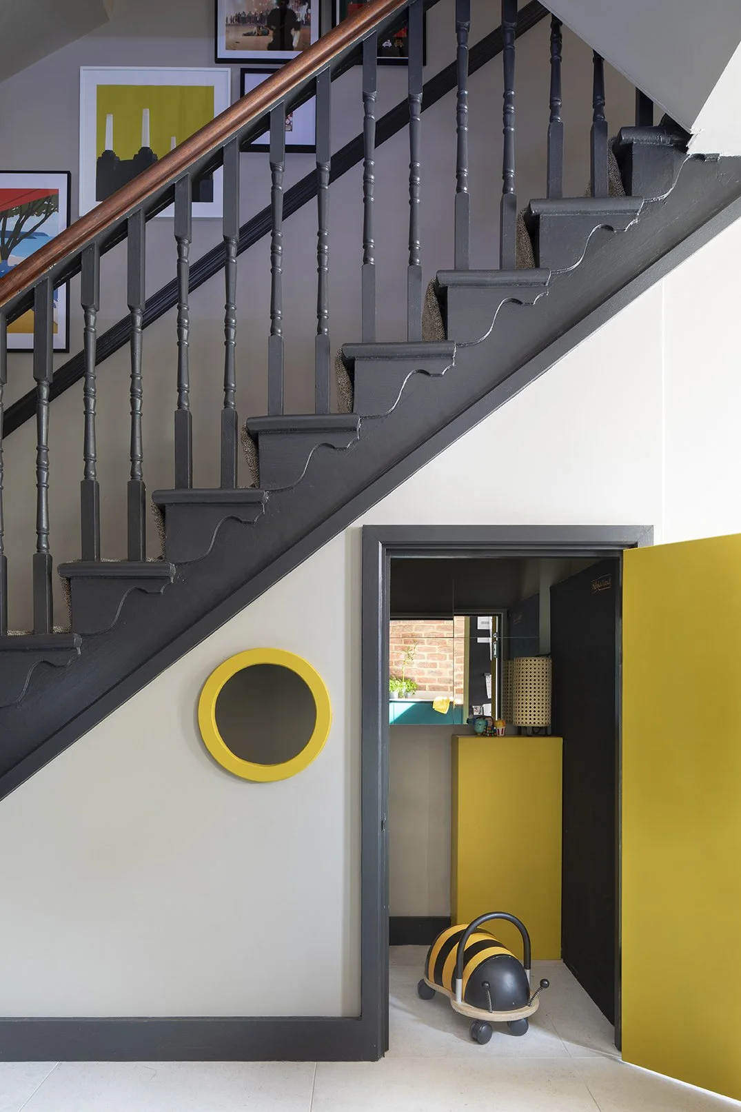 Under-stairs children's playroom with the yellow painted door open in a North Shields family home by Carole Crowe Interior Design, revealing a compact yellow-lined play space with a view through to the kitchen beyond, a circular yellow-framed cat fla