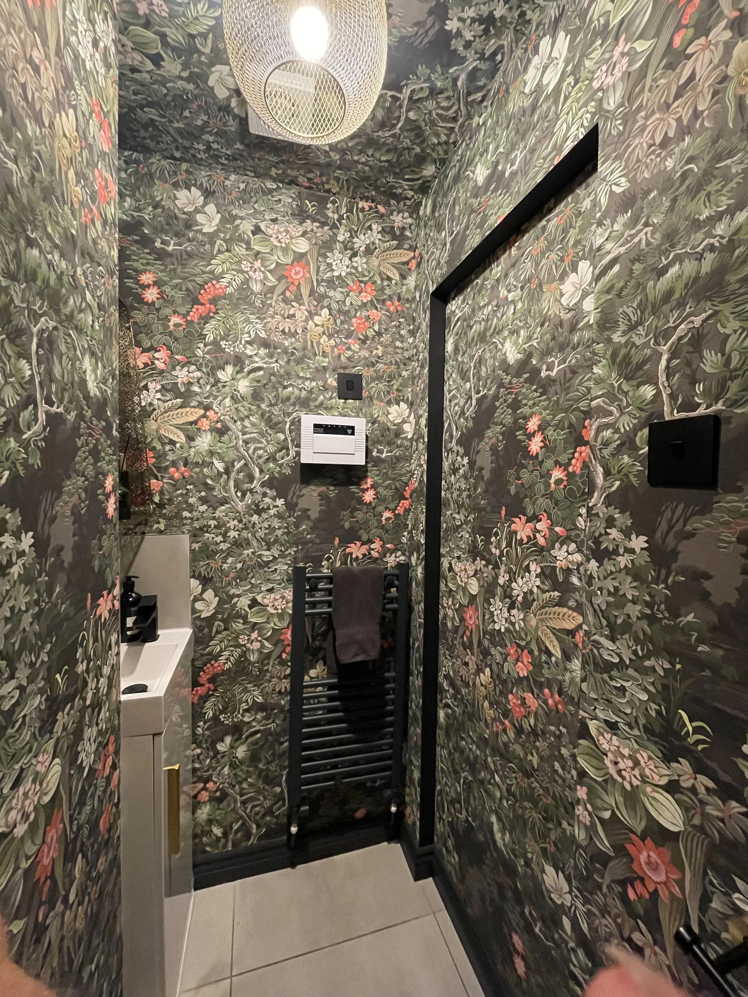 Dramatic downstairs cloakroom with dark floral wallpaper, black heated towel rail and wicker pendant light, Tynemouth