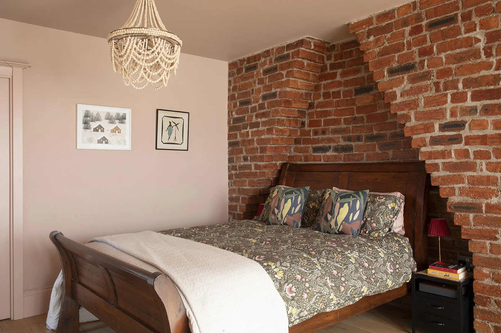 Wide view of the bedroom in the Queens Road project by Carole Crowe Interior Design, Whitley Bay, featuring a dark wood sleigh bed with William Morris-style dark floral bedspread and botanical print cushions set into the exposed red brick chimney bre