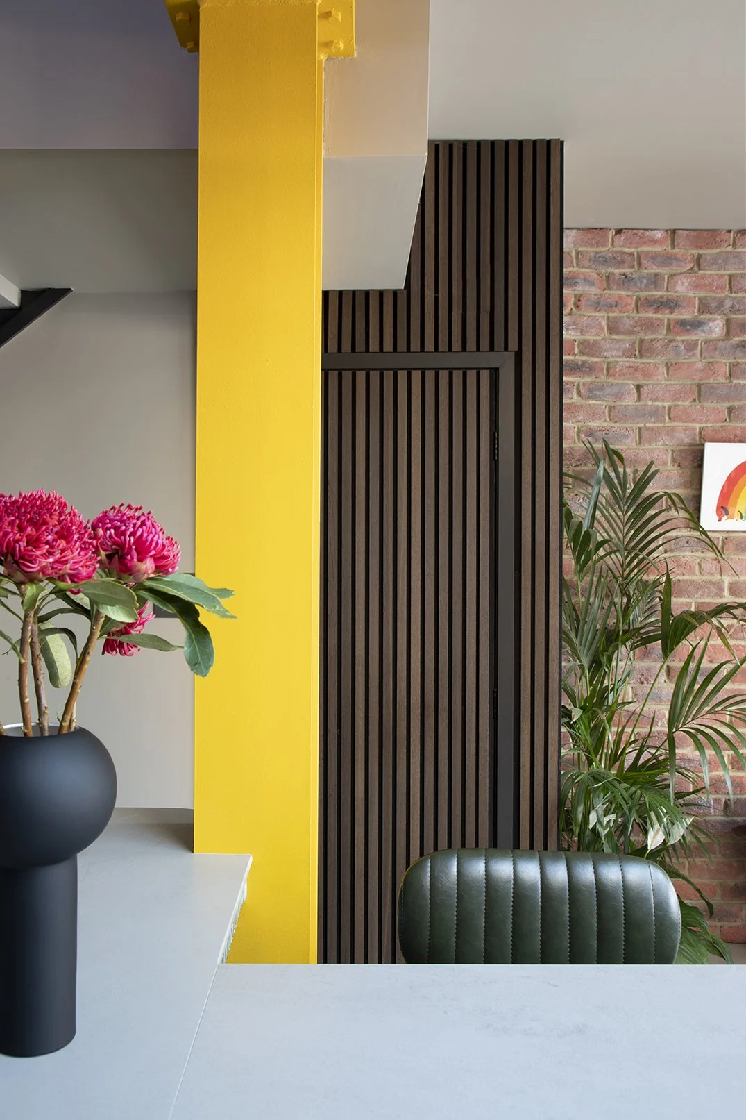View from the kitchen into the staircase hall of a North Shields family home designed by Carole Crowe Interior Design, featuring a painted black Victorian staircase with turned spindles and polished wood handrail, a densely hung gallery wall of frame
