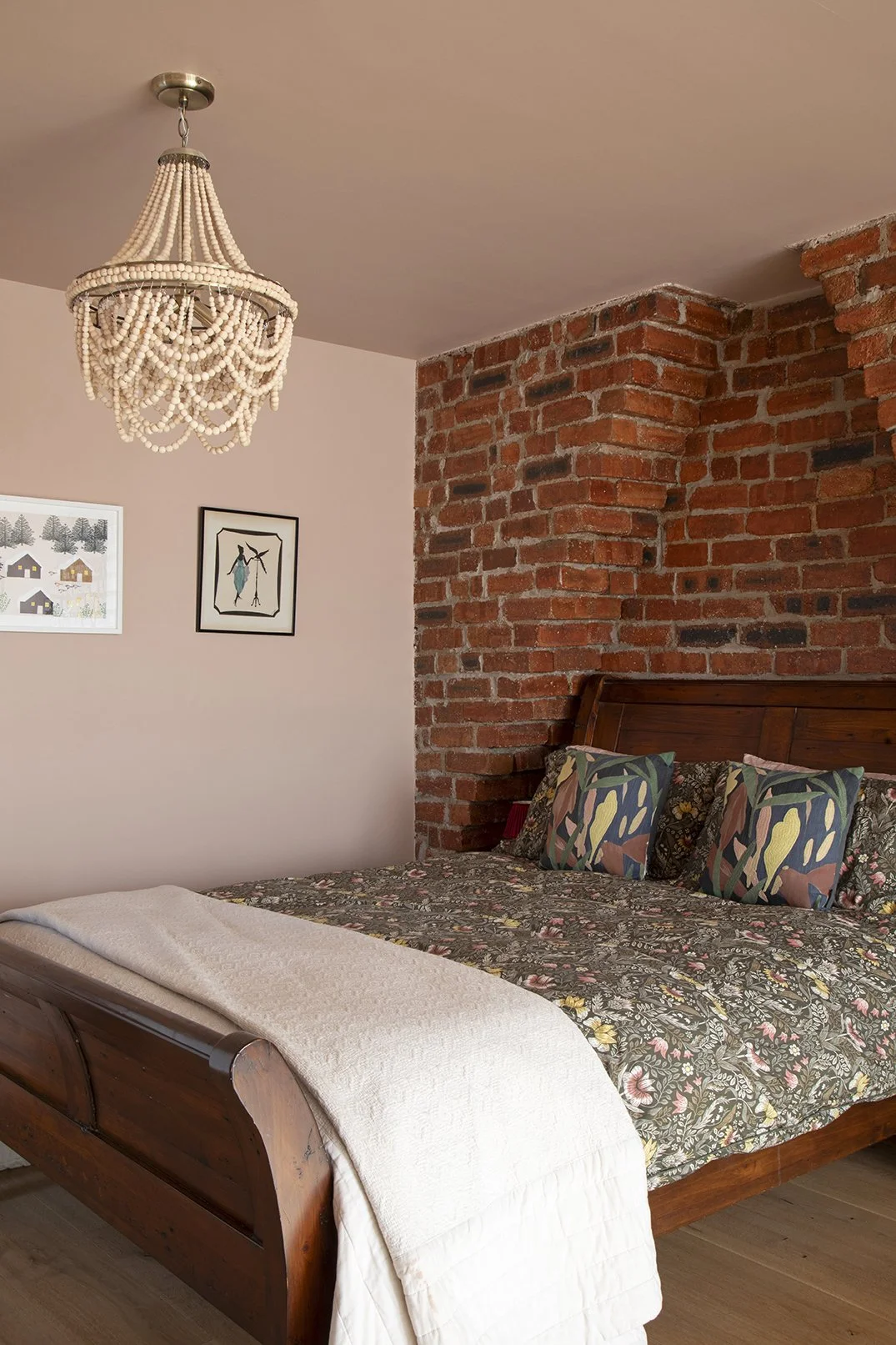 Bedroom overview in the Queens Road project by Carole Crowe Interior Design, Whitley Bay, showing a dark wood sleigh bed dressed with a William Morris-style dark floral bedspread and bold botanical print cushions against a raw exposed red brick chimn