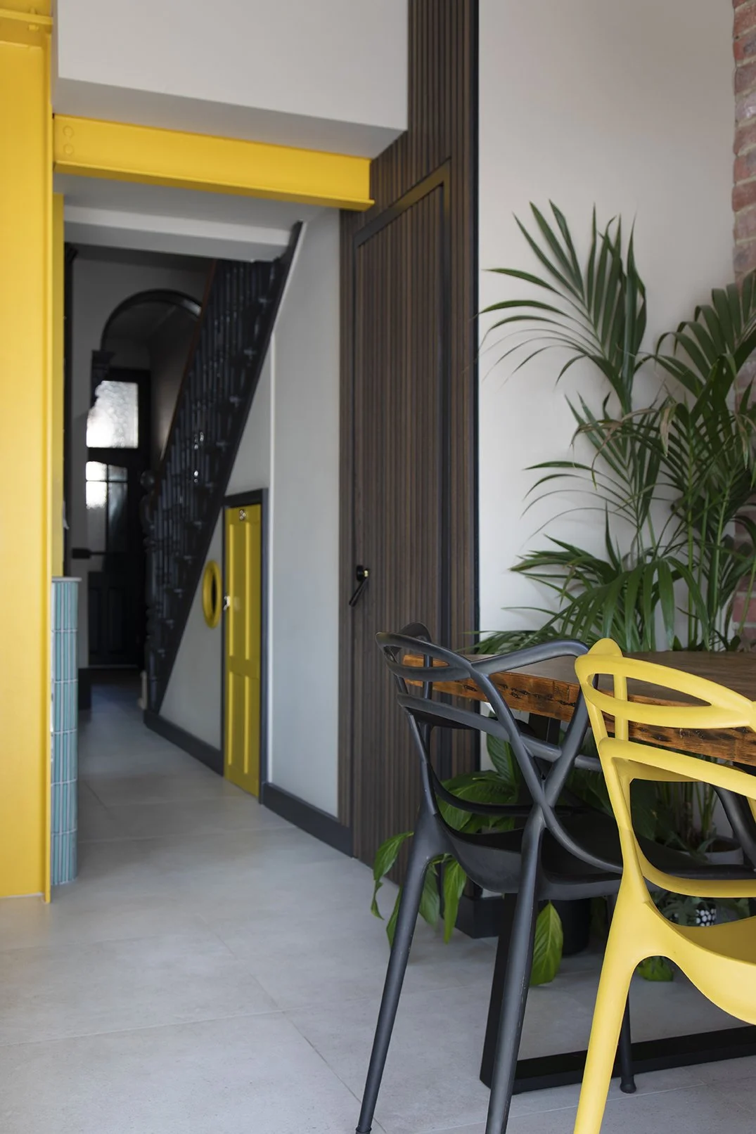 View from the dining area through the yellow painted structural steel portal frame towards the staircase hallway in a North Shields family home by Carole Crowe Interior Design, showing the dark timber slatted cloakroom door, painted black Victorian s