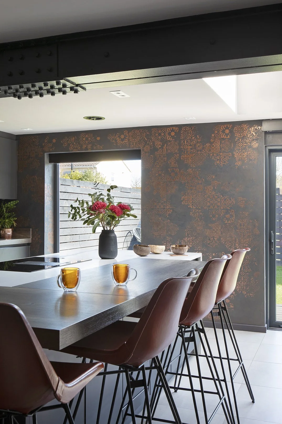 Full width kitchen island bar with tan leather stools, grey cabinets, copper Venetian plaster on two walls and exposed painted steel RSJ beam, Lytham Road Whitley Bay