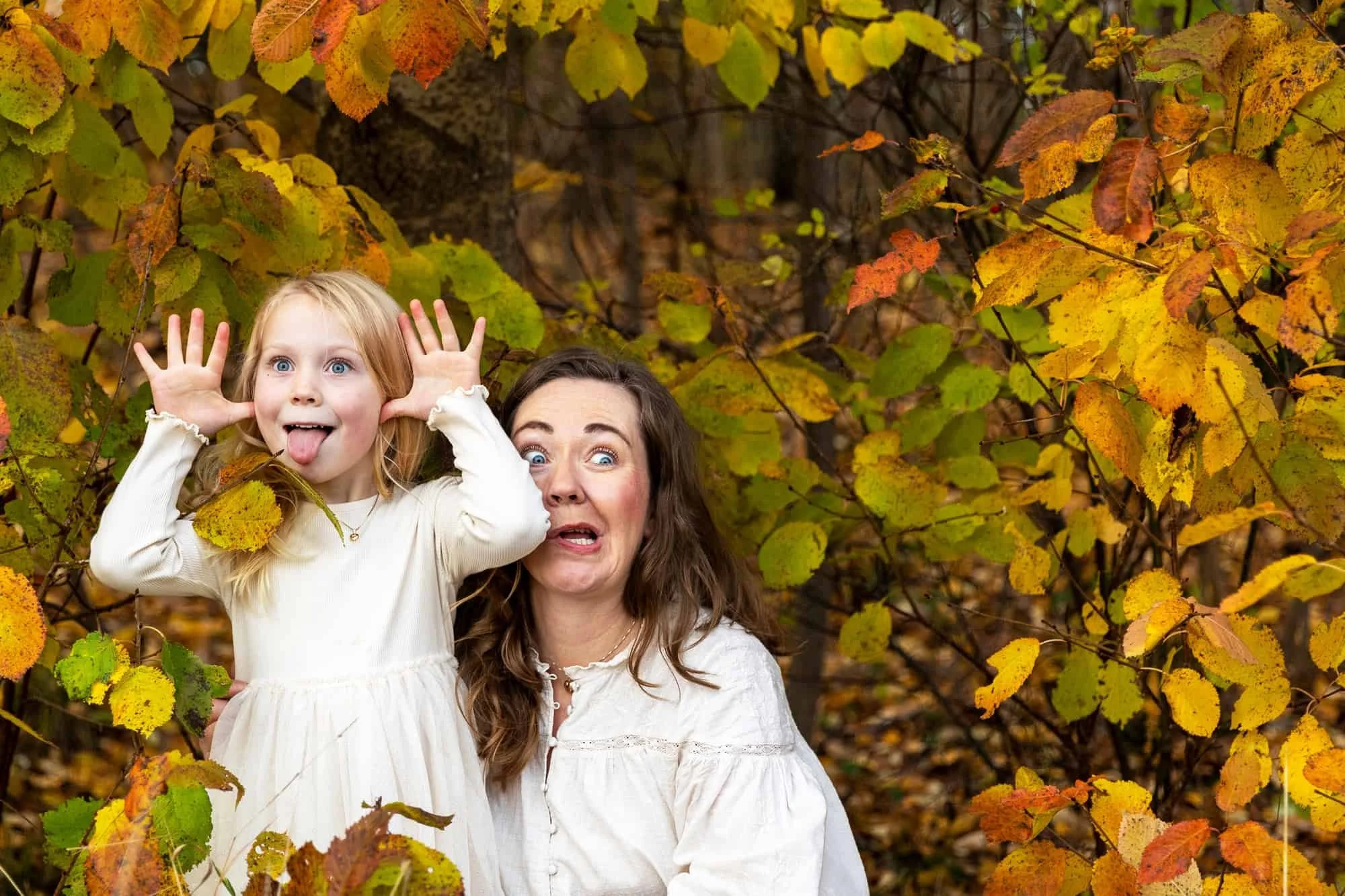 Mor og datter kledd i hvitt gjør grimaser blant høstløv