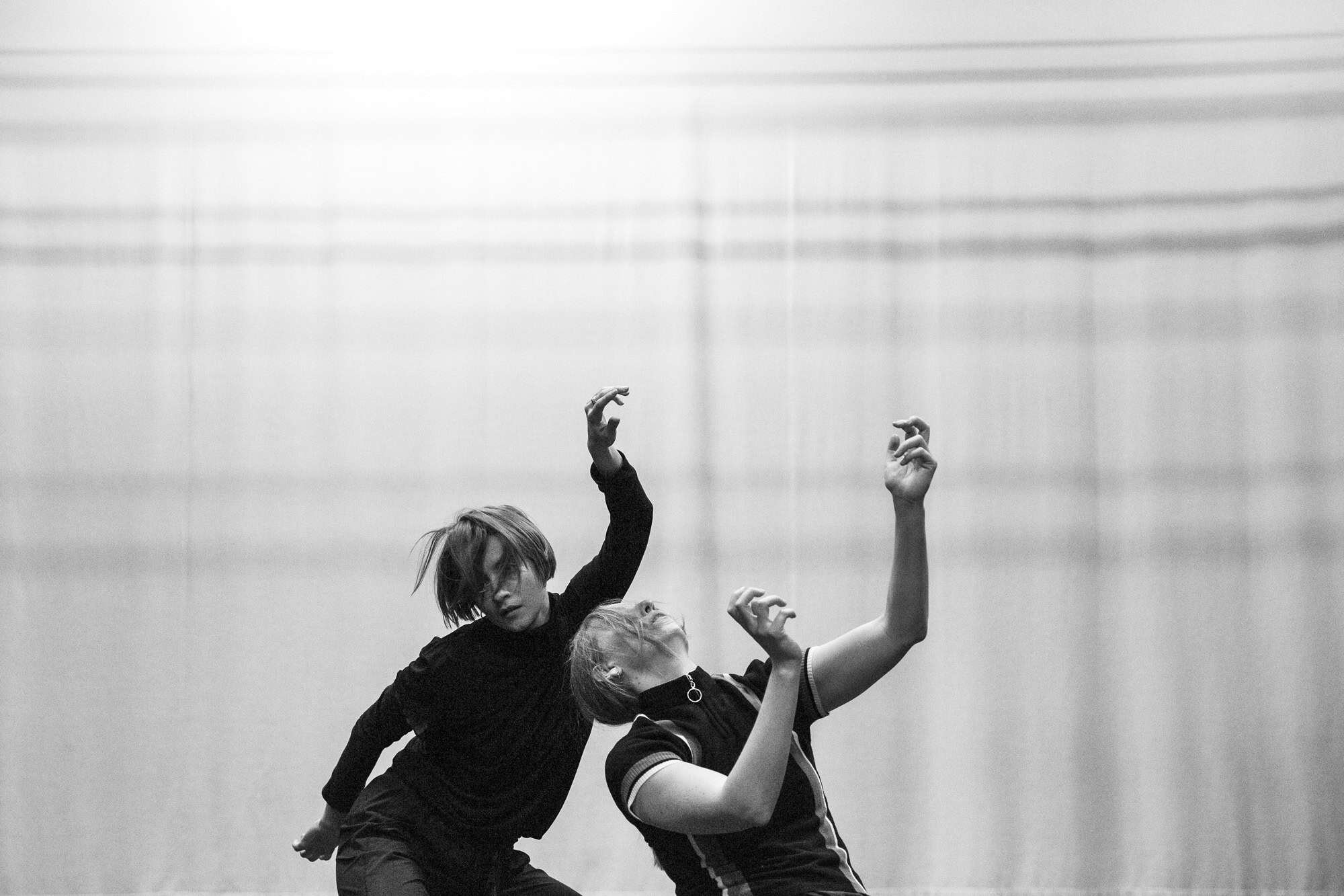 To dansere med krøkete hender i lufta mot en bakgrunn av vertikale og horisontale striper