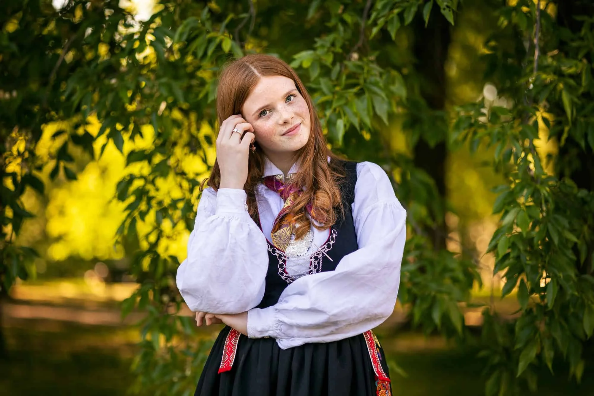 Konfirmant med rødt hår i bunad står foran et tre i Oslo