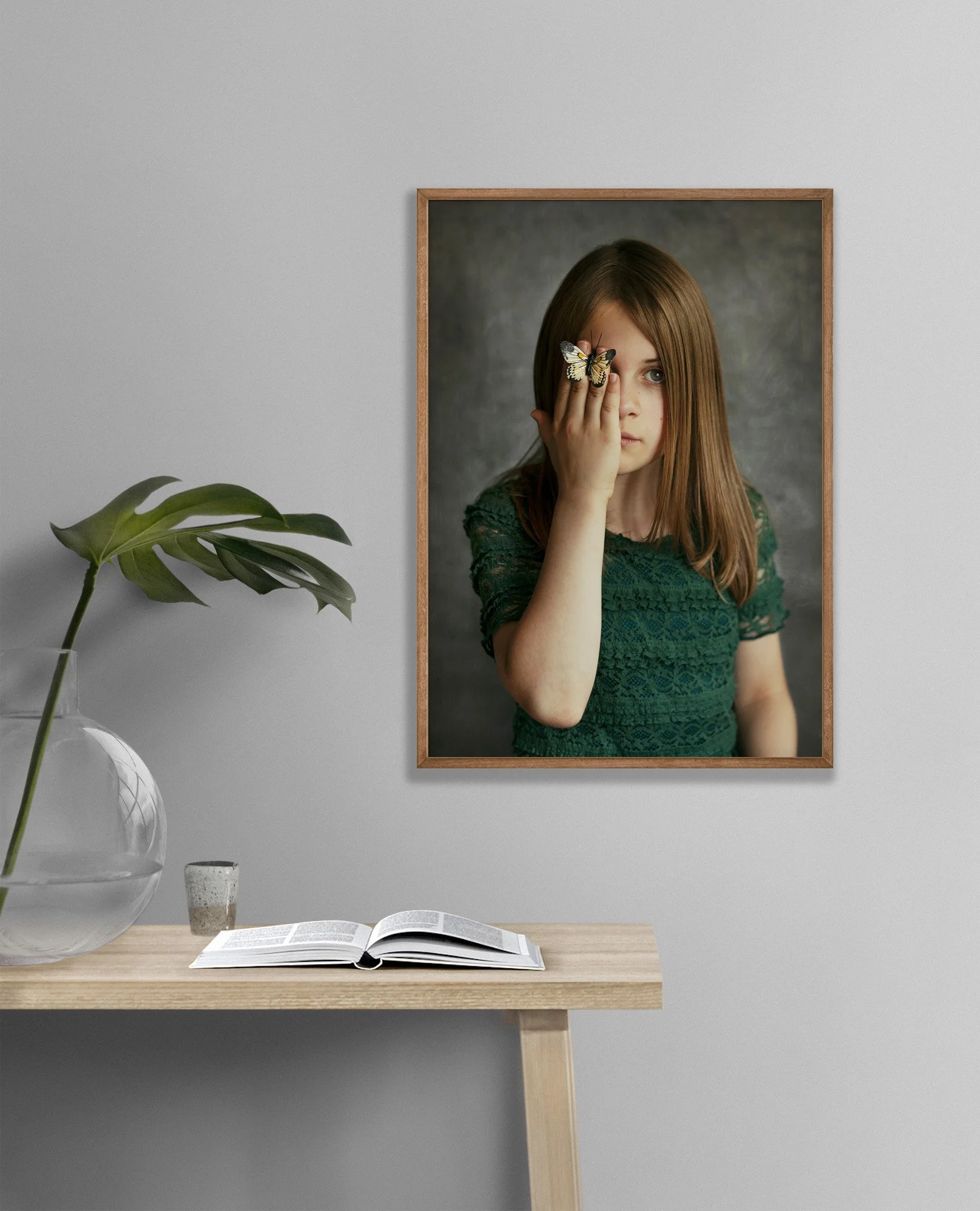 Portrett av jente i grønn kjole som holder en sommerfugl foran det ene øyet, avbildet i en ramme på veggen.