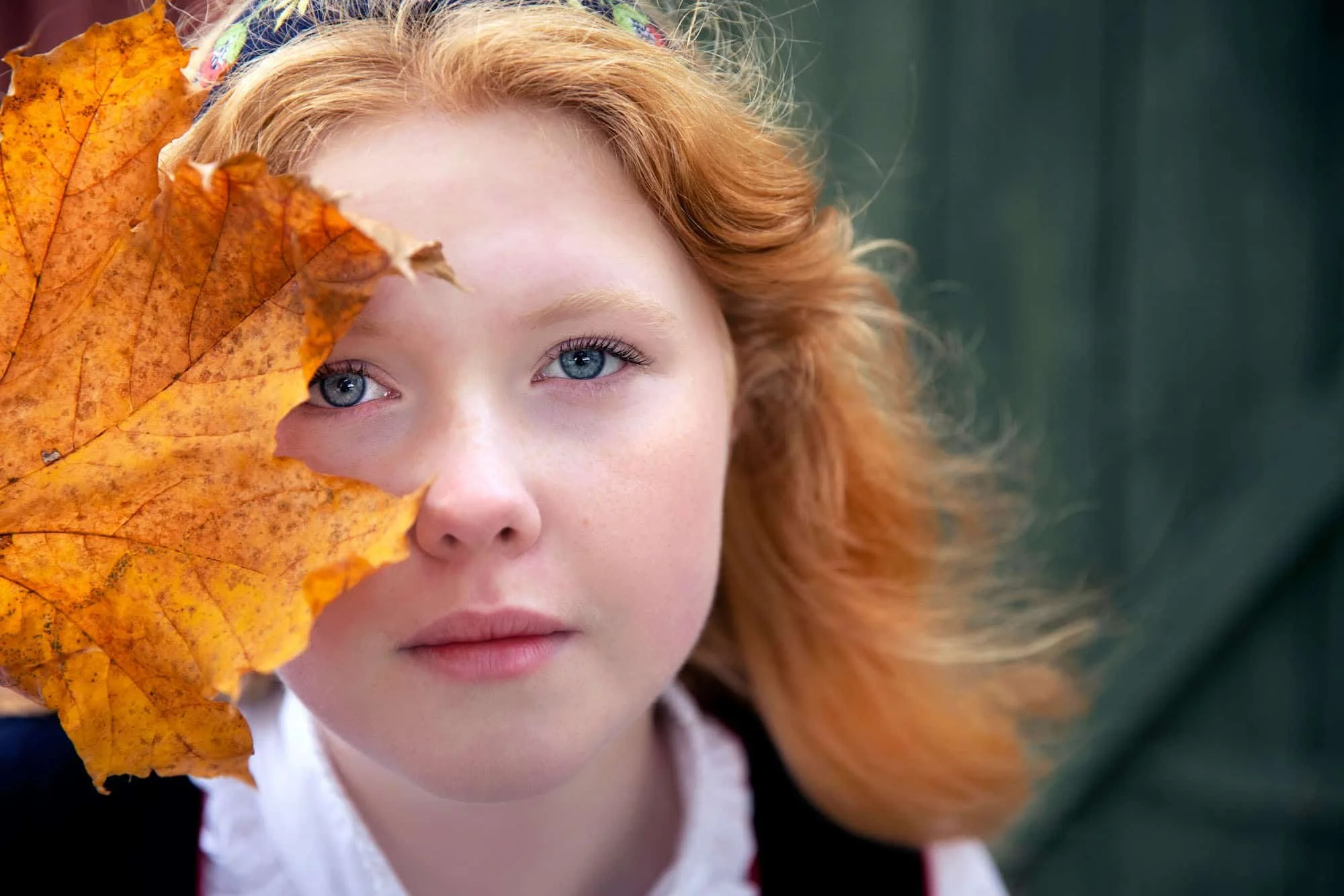 Portrett av konfirmant fotografert utendørs med et stort gul blad på siden av ansiktet – foto Kristin Opdan