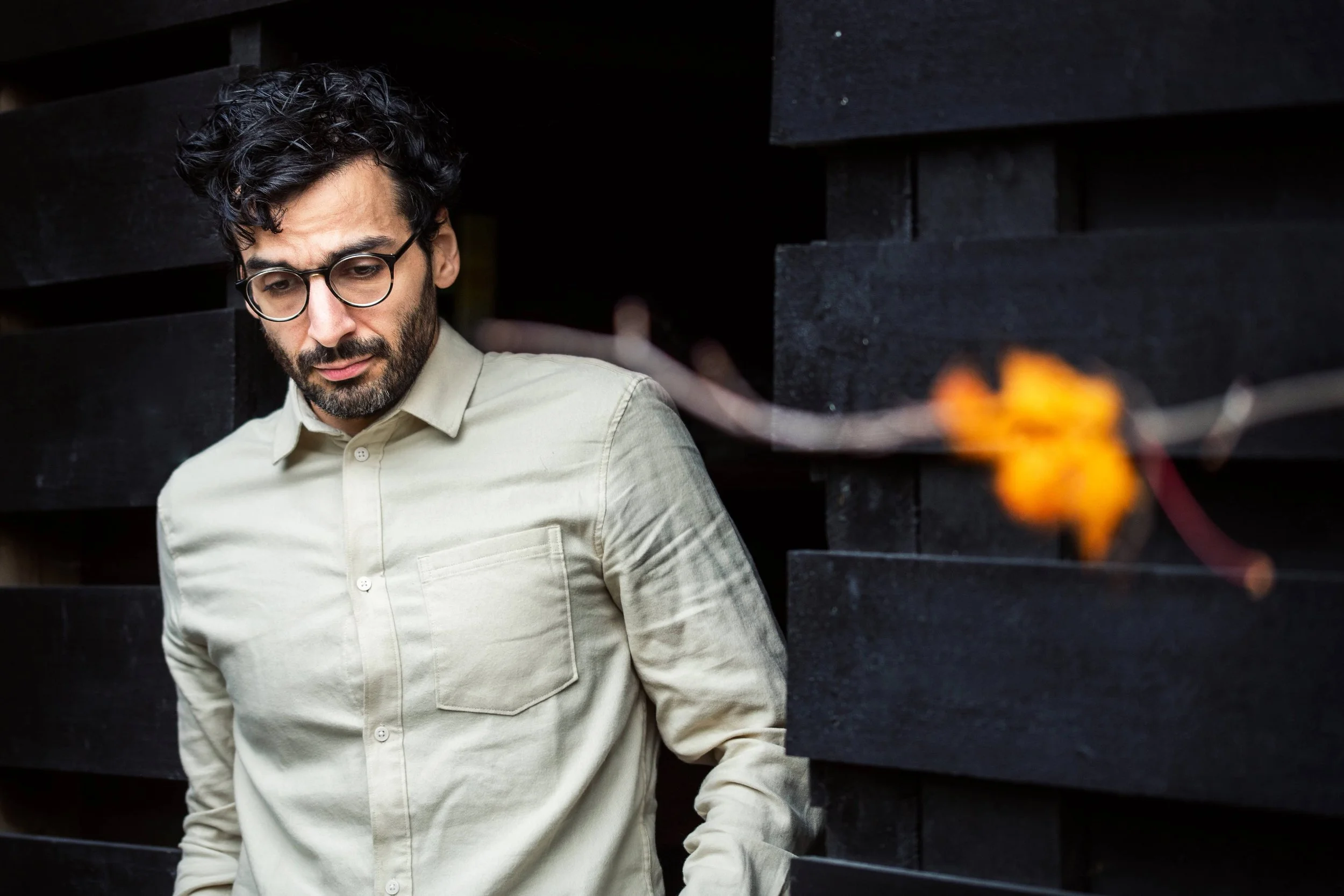 Portrettfotografering av mann i hvit skjorte som ser ned i bakken med en uskarp grein med et orange blad til høyre i bildet