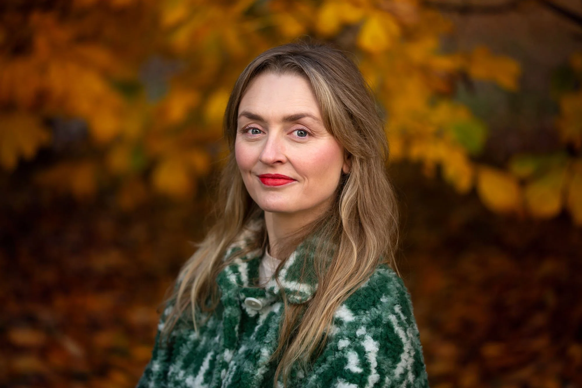 Kvinne med rød leppestift og grønn jakke i en skog i høstfarger