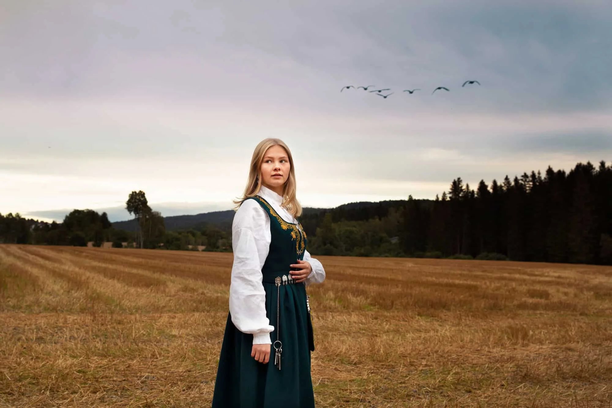 Konfirmant fotografert i åpent landskap med himmel og fugler i bakgrunnen