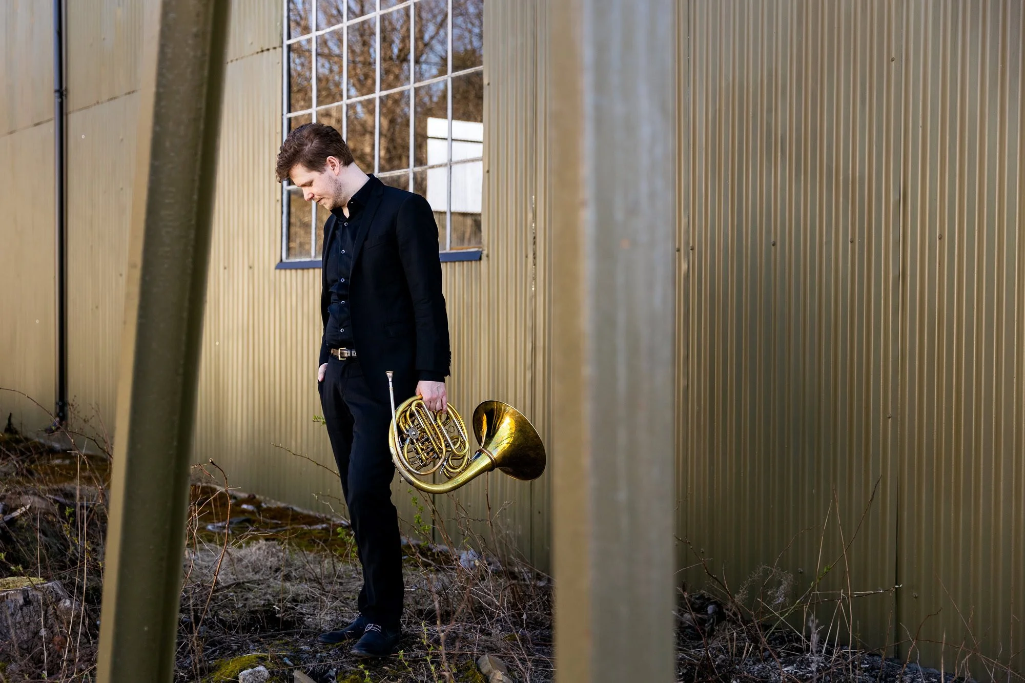 Hornist Simen Hagen fotografert i industrielt miljø på Gressholmen, med et alvorlig uttrykk.