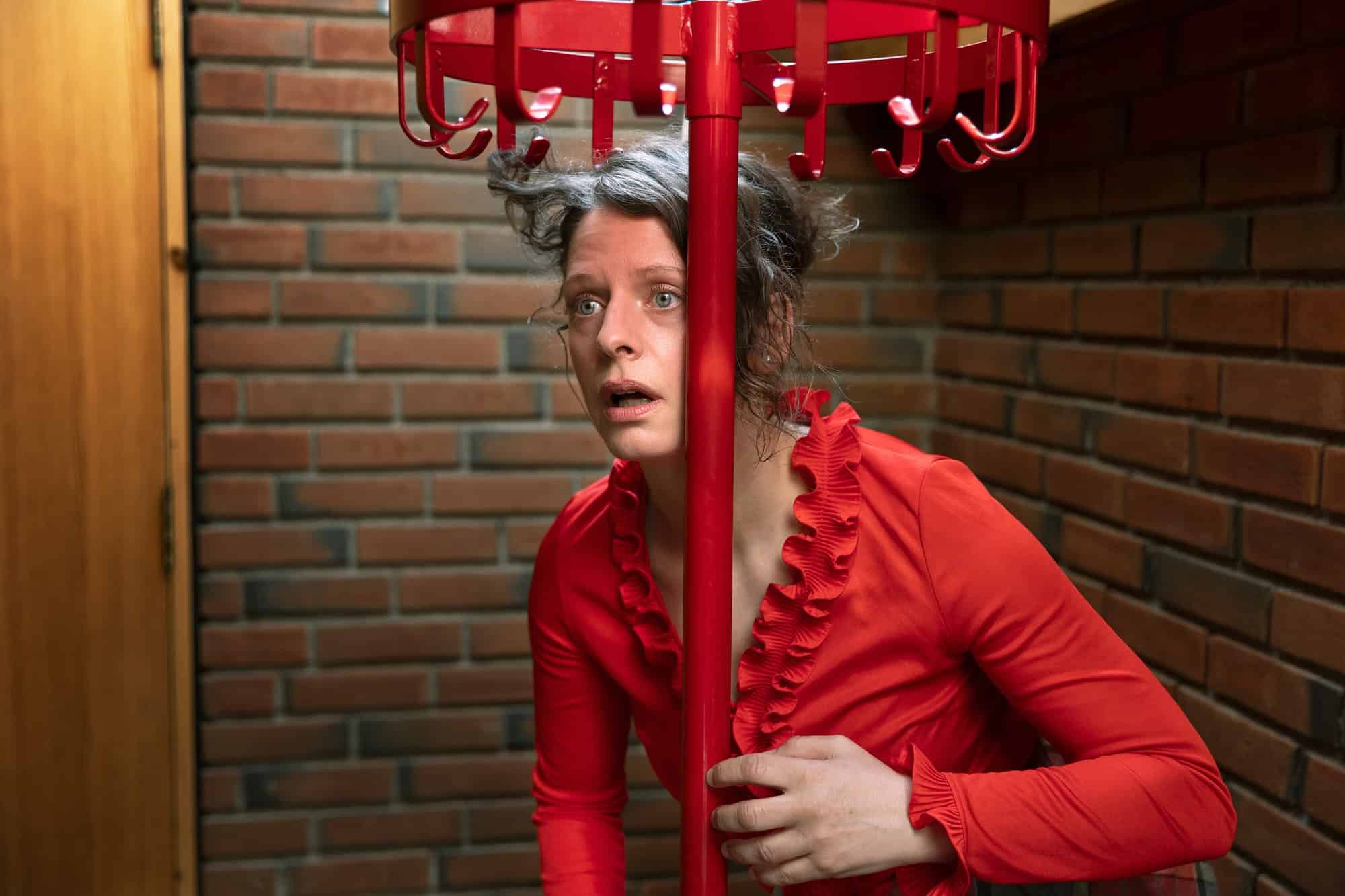 Kreativt portrett av skuespiller hengende fast i rød knagg mot murvegg på Oppsal Samfunnshus.