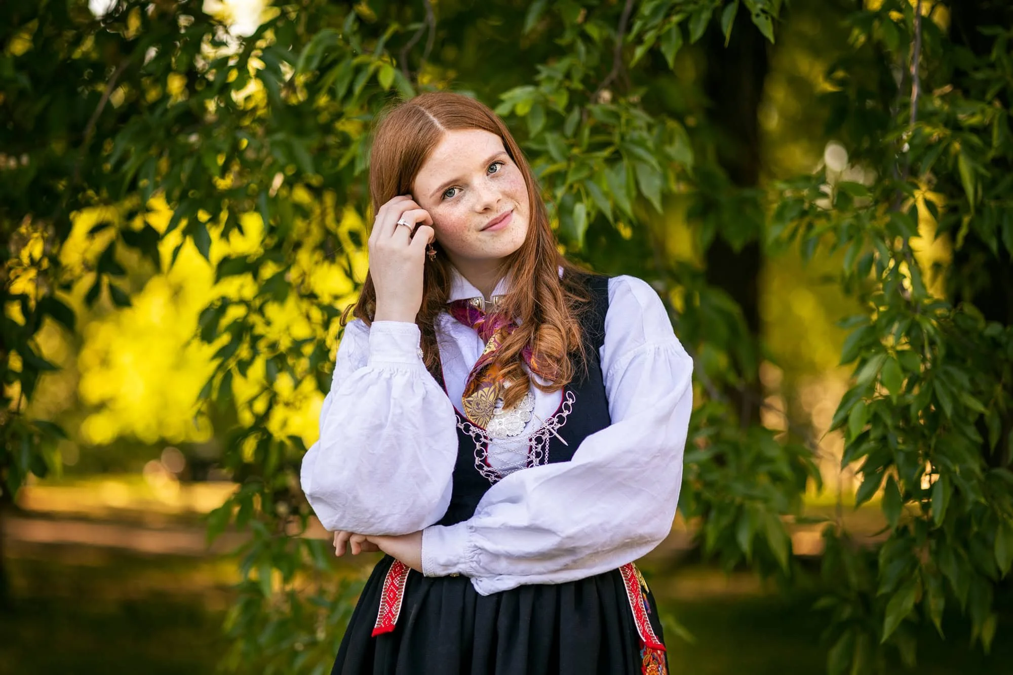 Nært portrett av konfirmant i grønne omgivelser under konfirmantfotografering