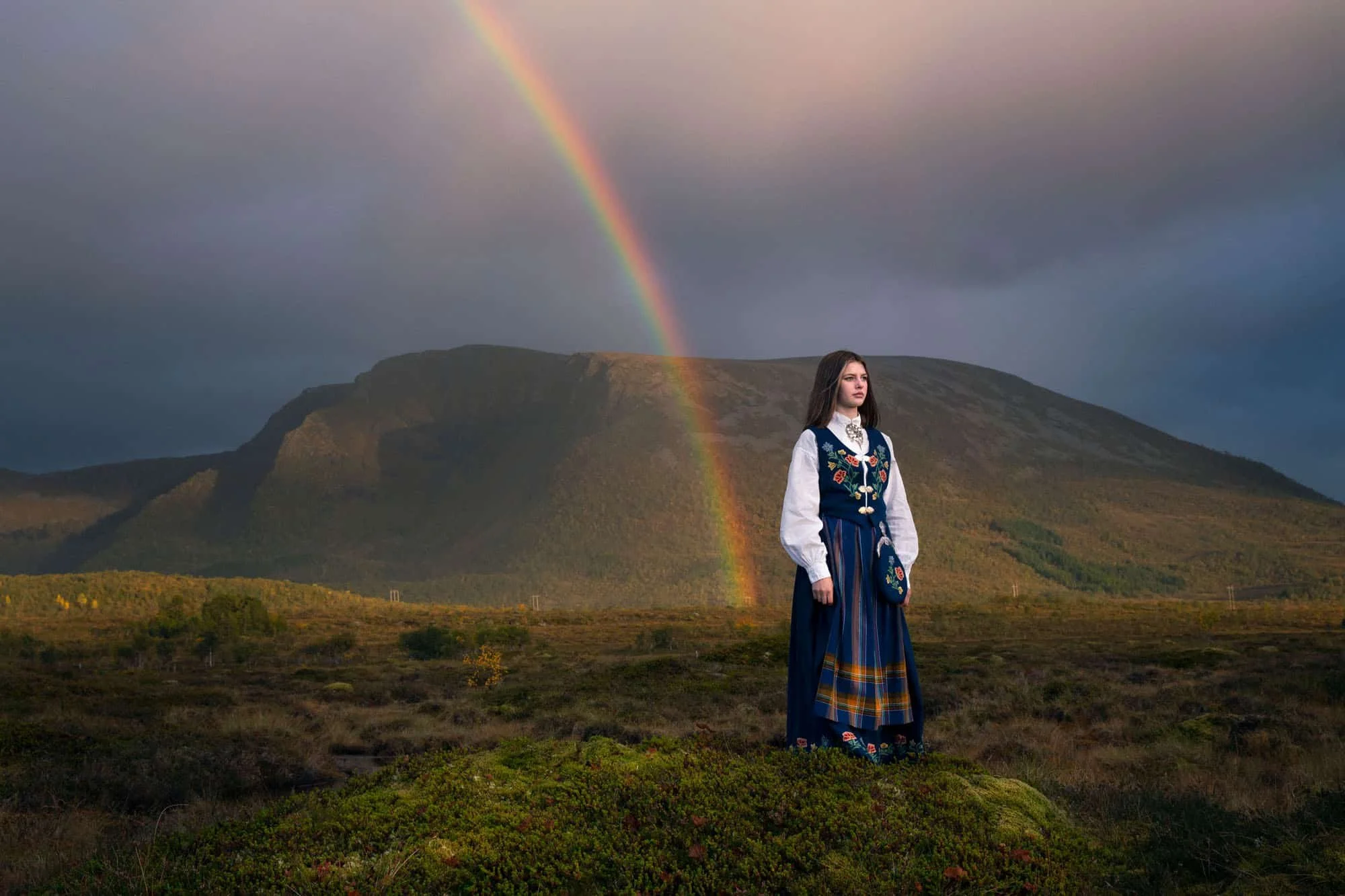 Konfirmant ute i naturen med regnbue på himmelen