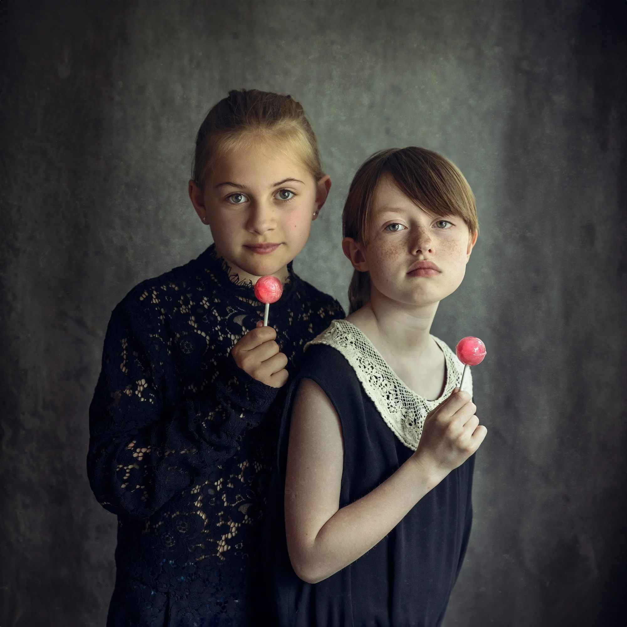 Kunstnerisk bilde av to jenter som holder en rosa kjærlighet på pinne, begge kledd i sorte blondekjoler