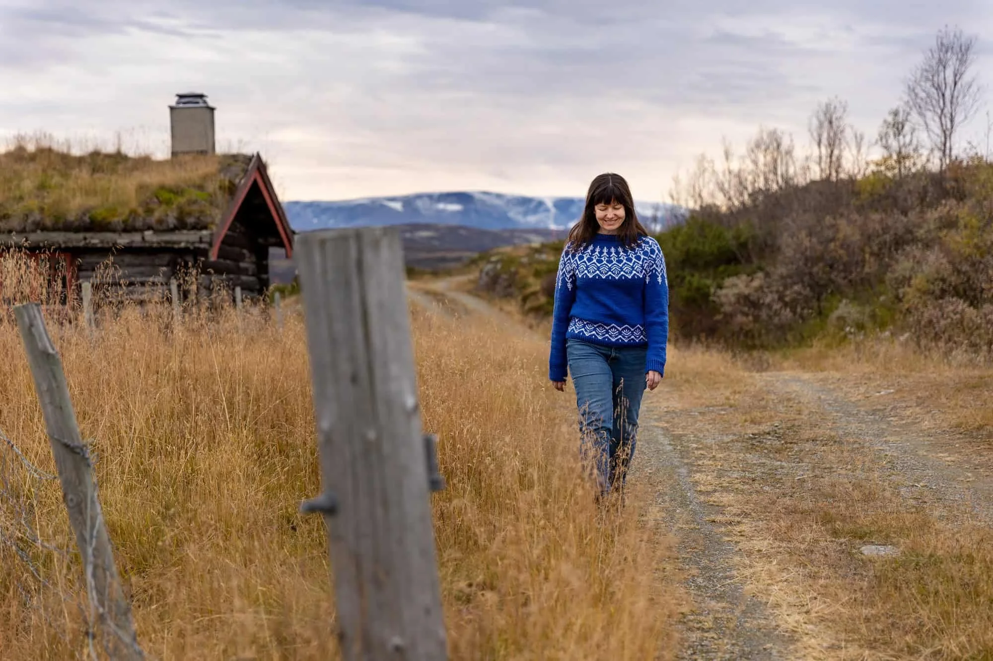 Kvinne går langs en sti i høstlandskap med fjell i bakgrunnen, fotografert utendørs i naturlig lys.