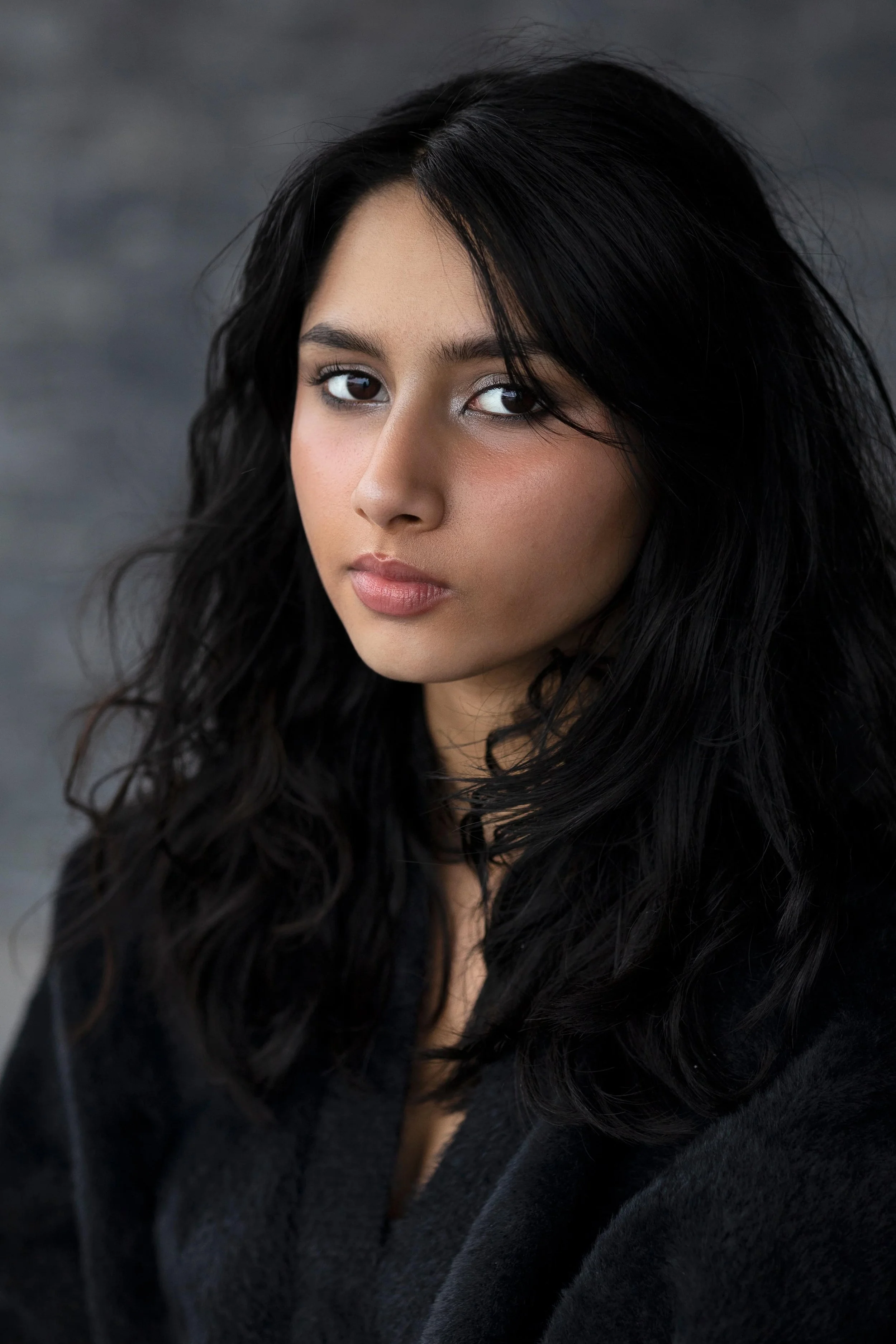 Ung, mørkhåret kvinne kledd i sort mot uskarp, grå bakgrunn
