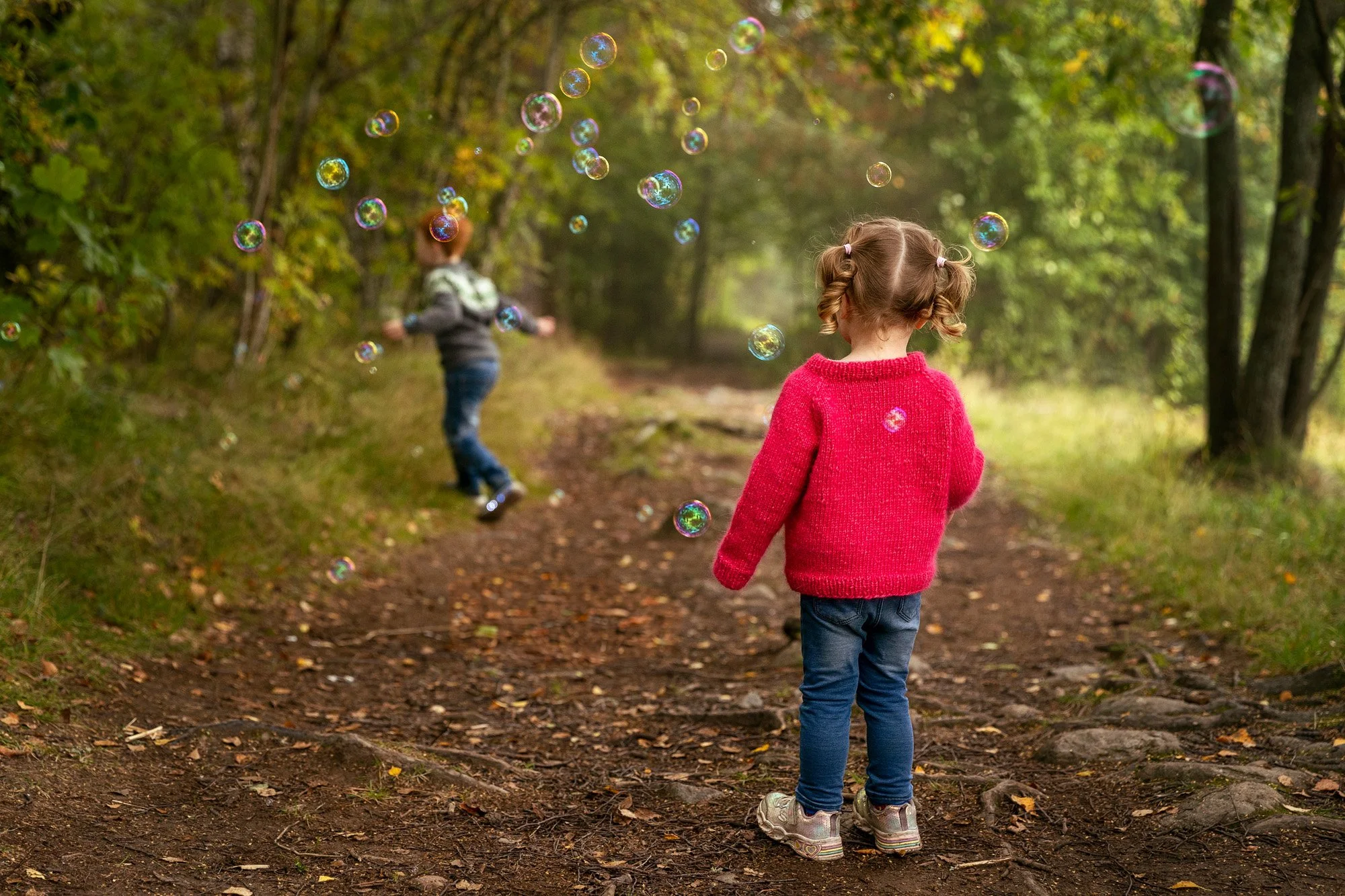Stemningsfullt familiebilde av barn fotografert bakfra i skogen på Oppsal omgitt av såpebobler – fotograf Kristin Opdan