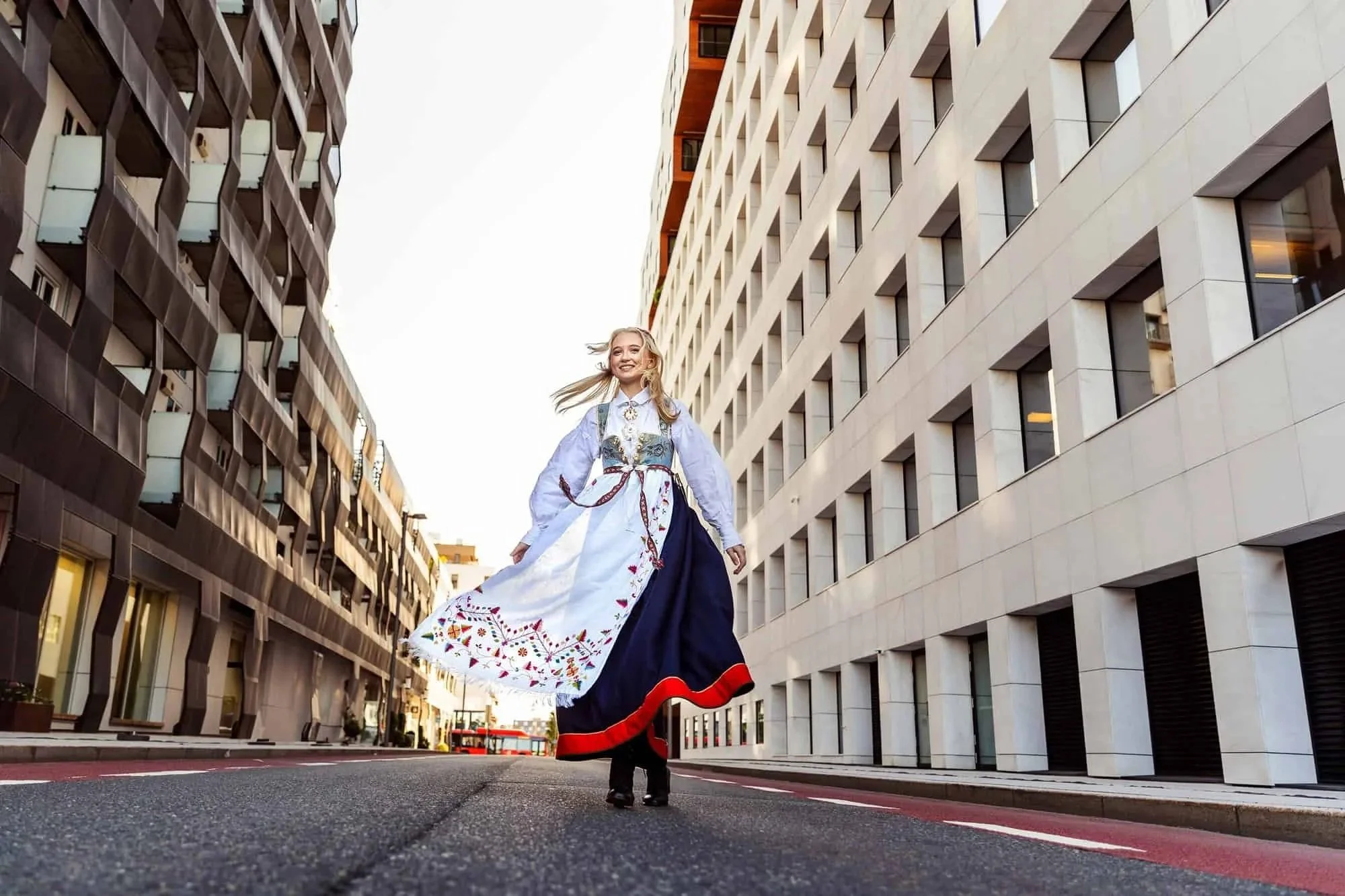 Bunadskledd jente snurrer rundt i bymiljø med høye hus på hver side
