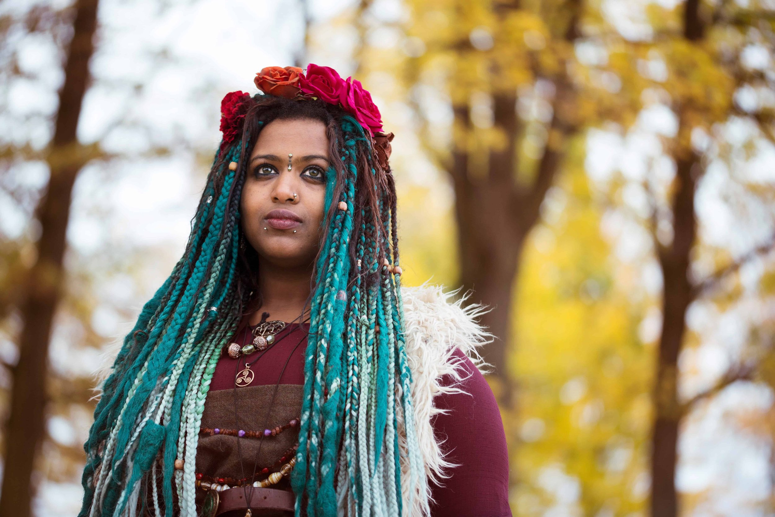 Kvinne med grønne rastafletter og røde blomster i håret med høstlige farger i bakgrunnen