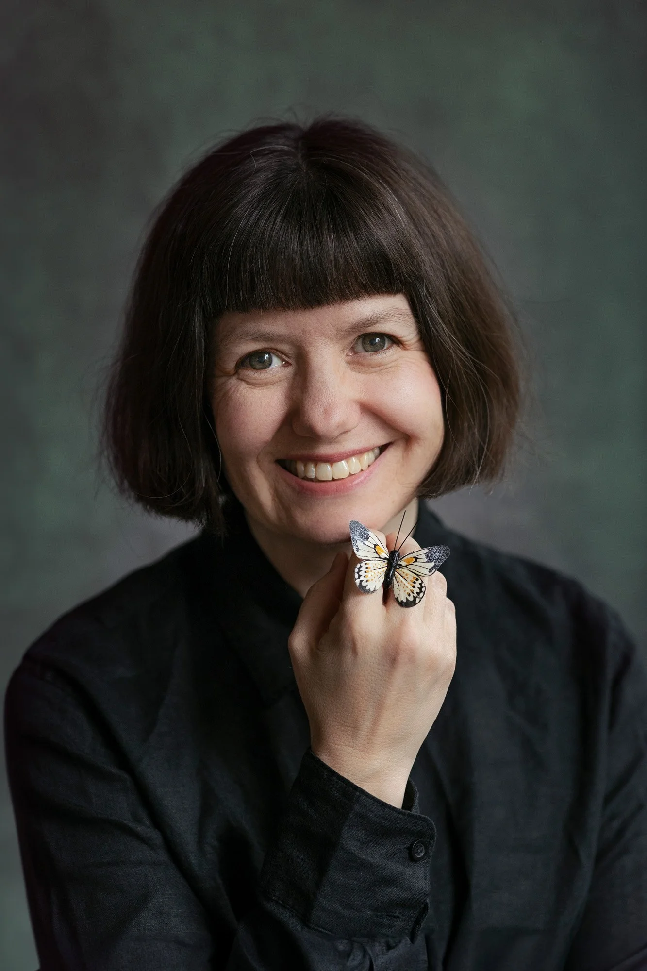 Smilende fotograf kledd i sort med en sommerfugl på hånden