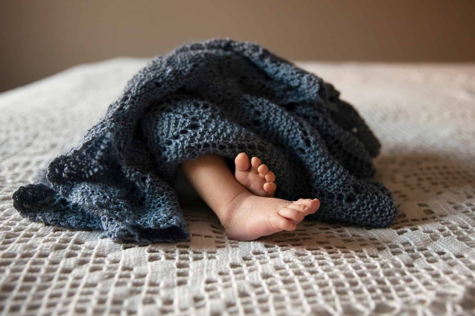 To babyføtter stikker ut av et blått strikket teppe