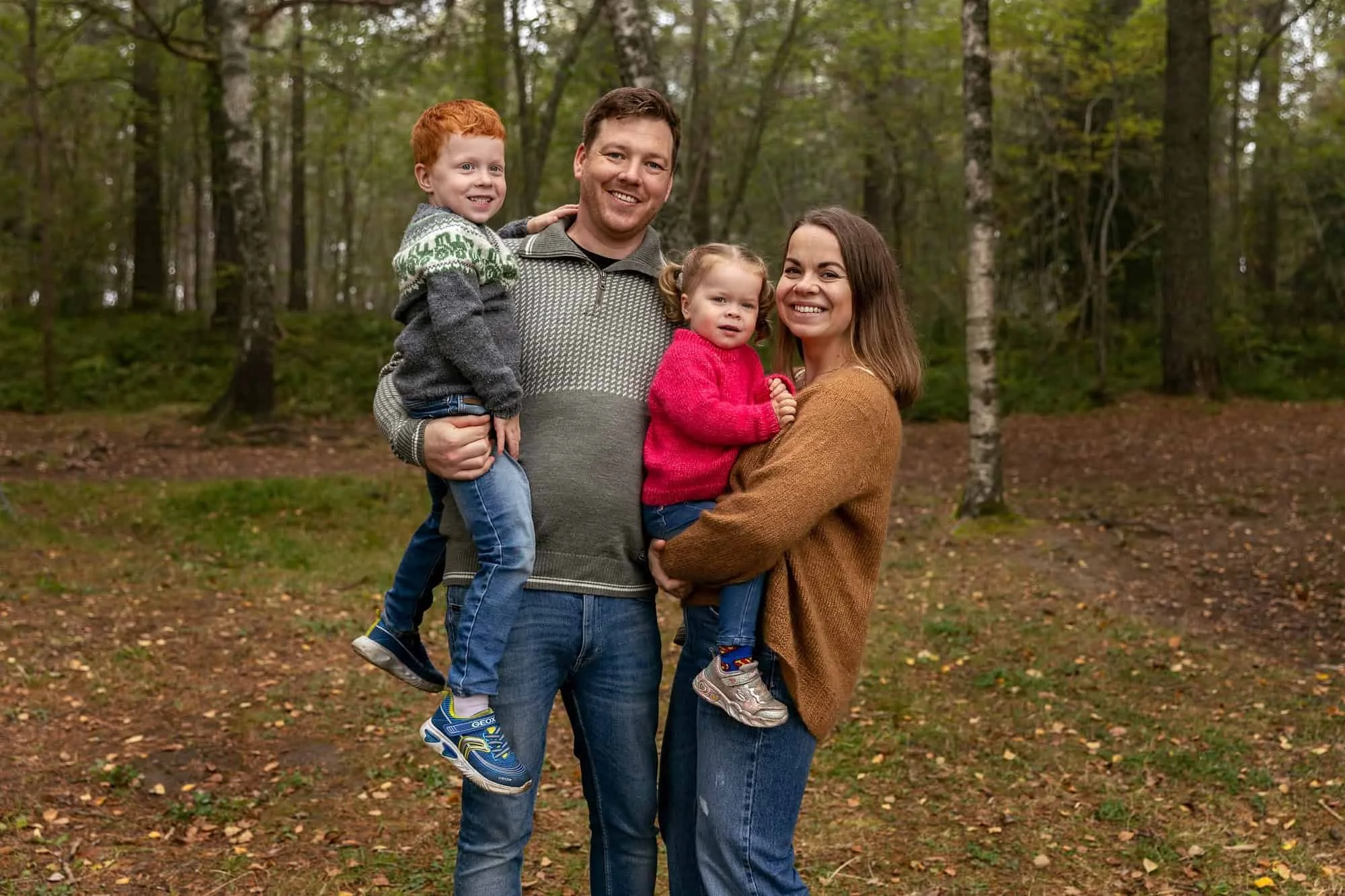 Blid familie i skogen med mor, far og to barn som ser i kamera