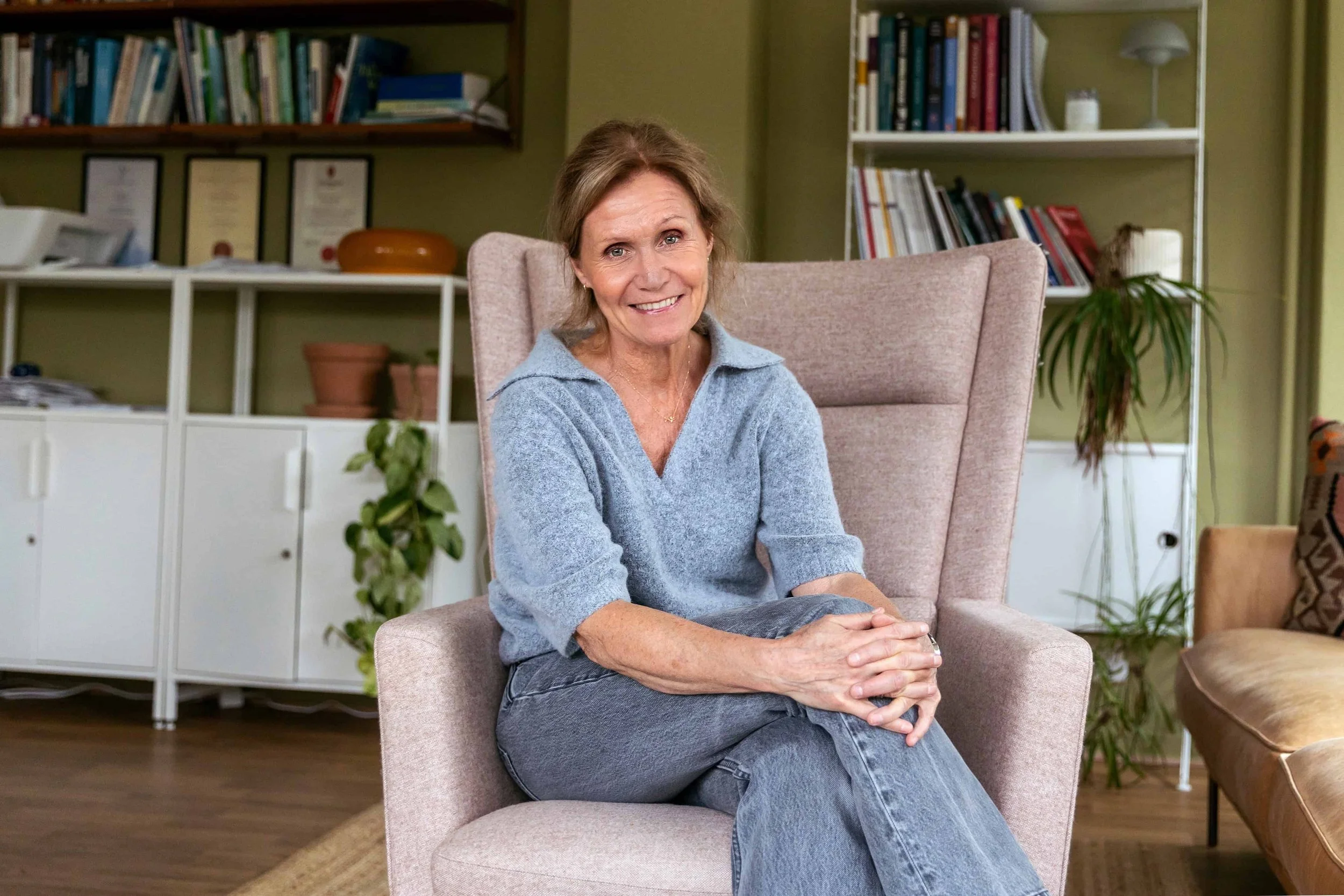 Blid terapeut sitter i en beige lenestol i en blå ullgenser