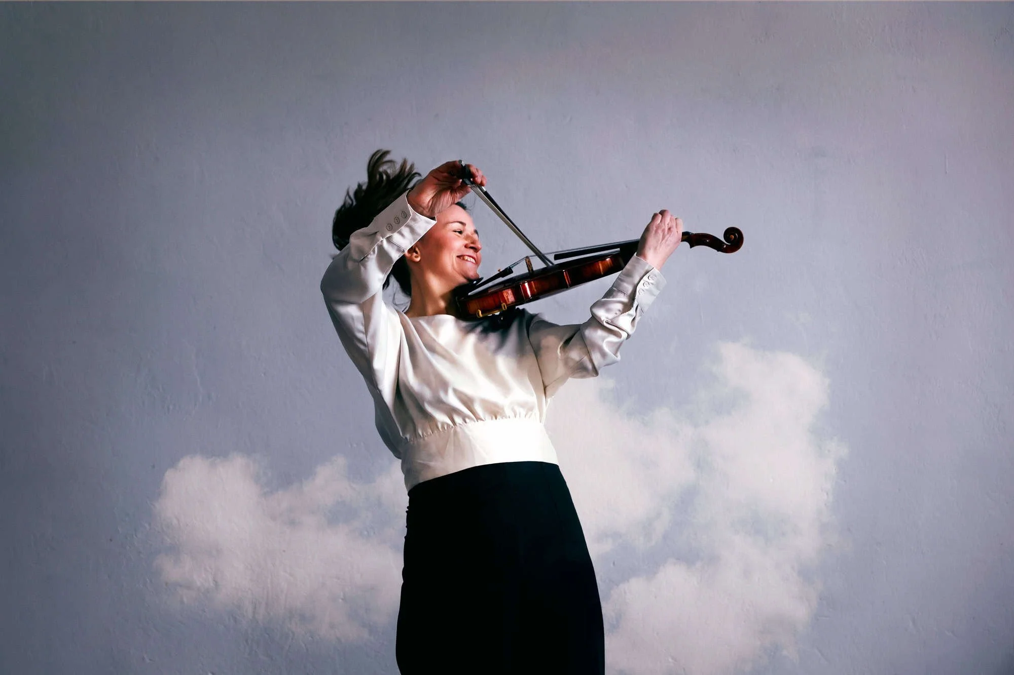 Blid fiolinst med bevegelse i håret fotografert mot en bakgrunn av hvite skyer