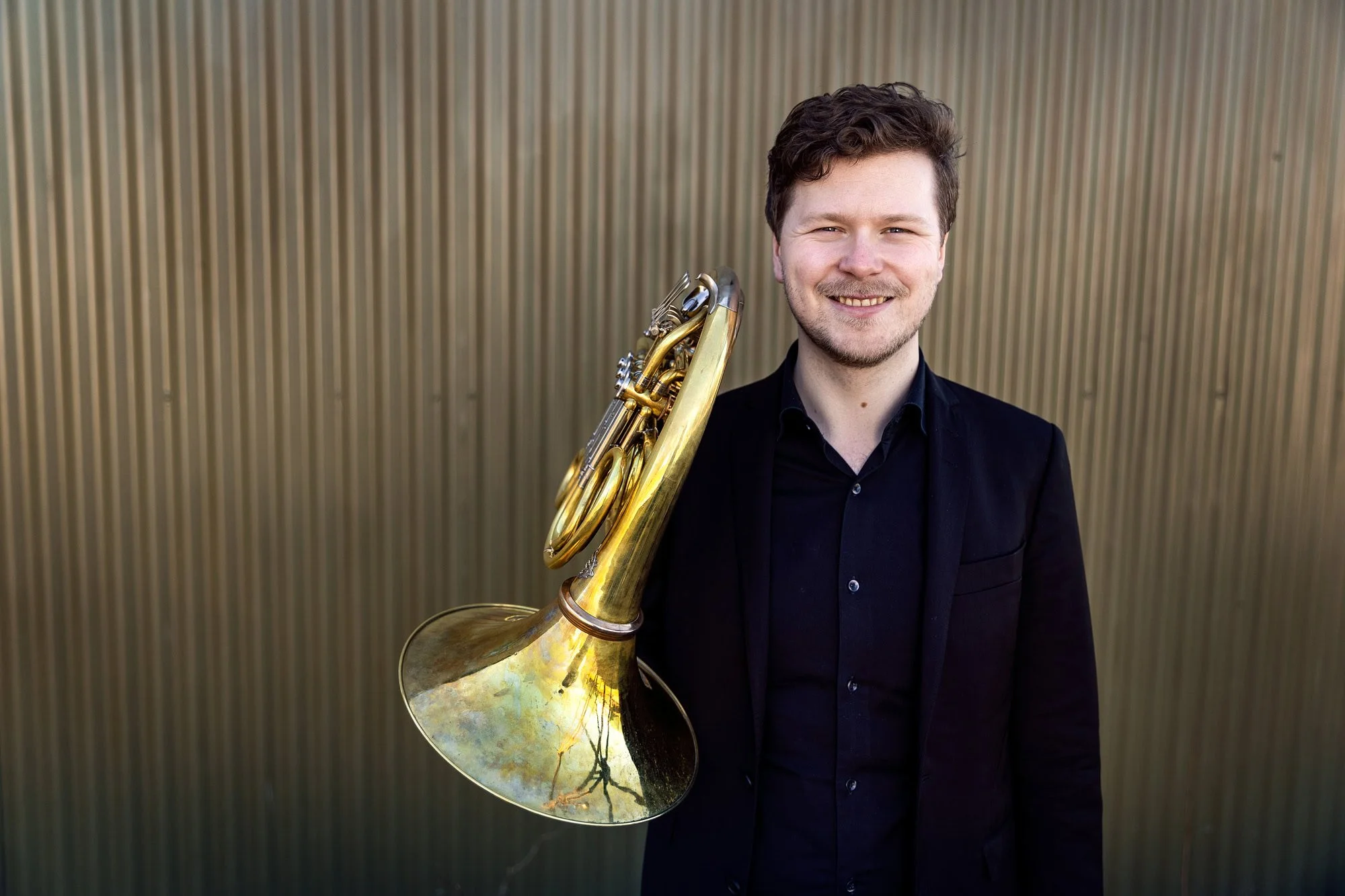 Portrett av hornist Simen Hagen fotografert på location i Oslo, med instrumentet mot skulderen og industriell bakgrunn.