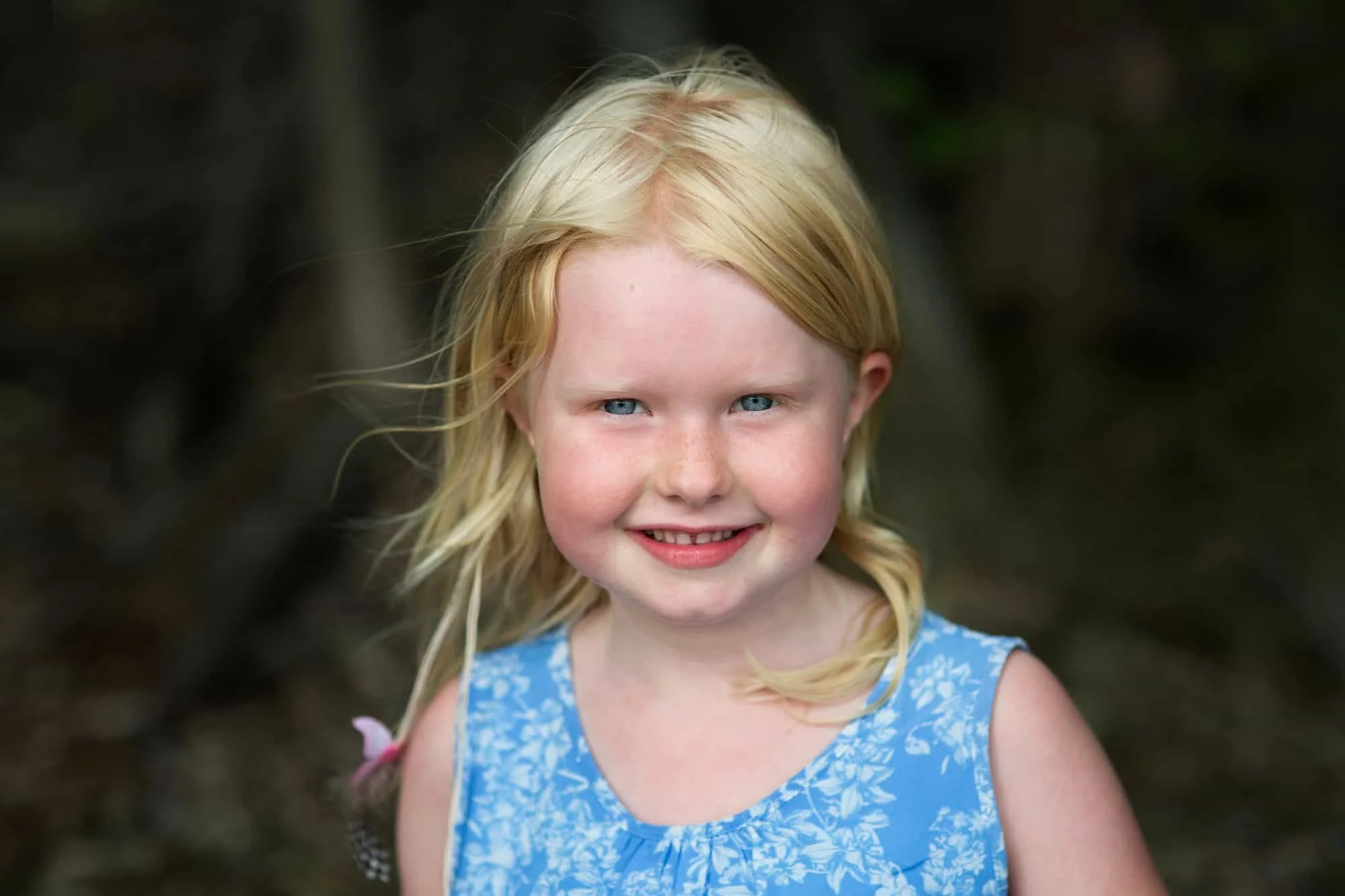 Blond jente i blå sommerkjole smiler og ser i kamera
