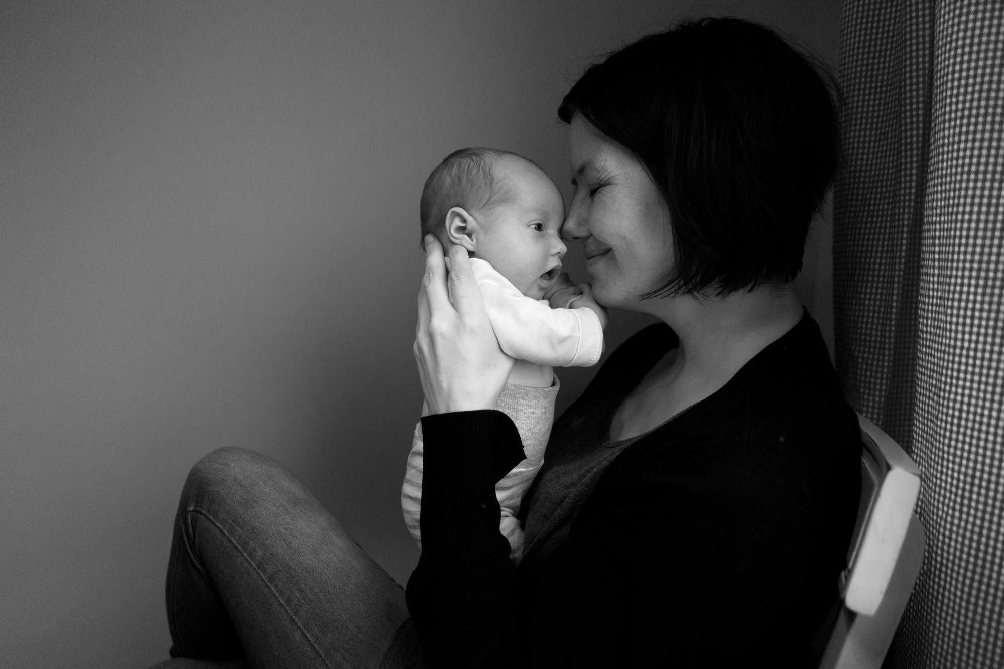 En mamma sitter i profil og holder barnet opp tett inntil seg