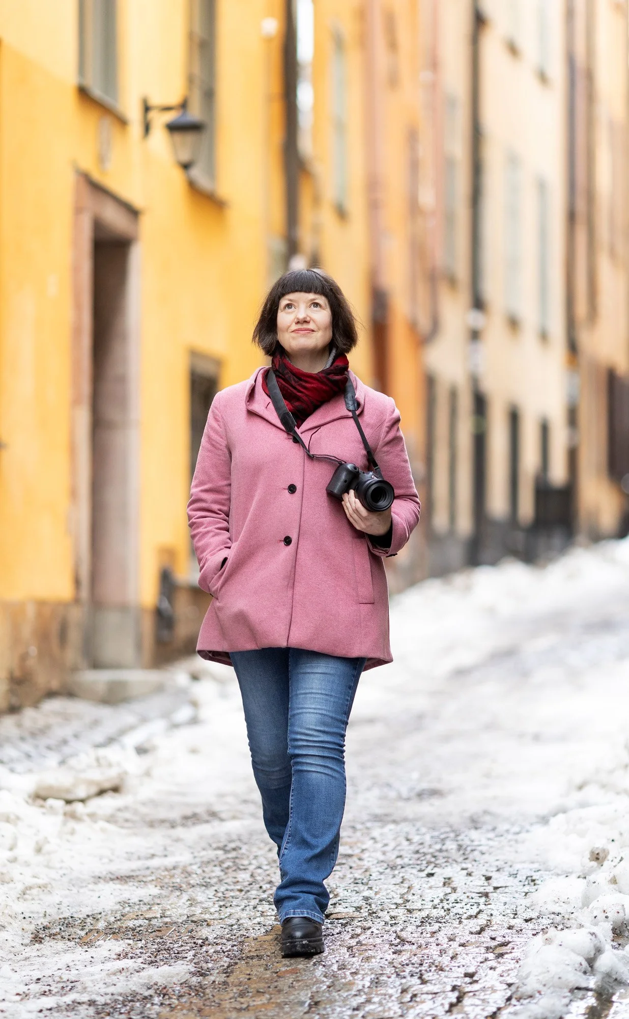 Gående kvinnelig fotograf i rosa jakke holder kamera under armene