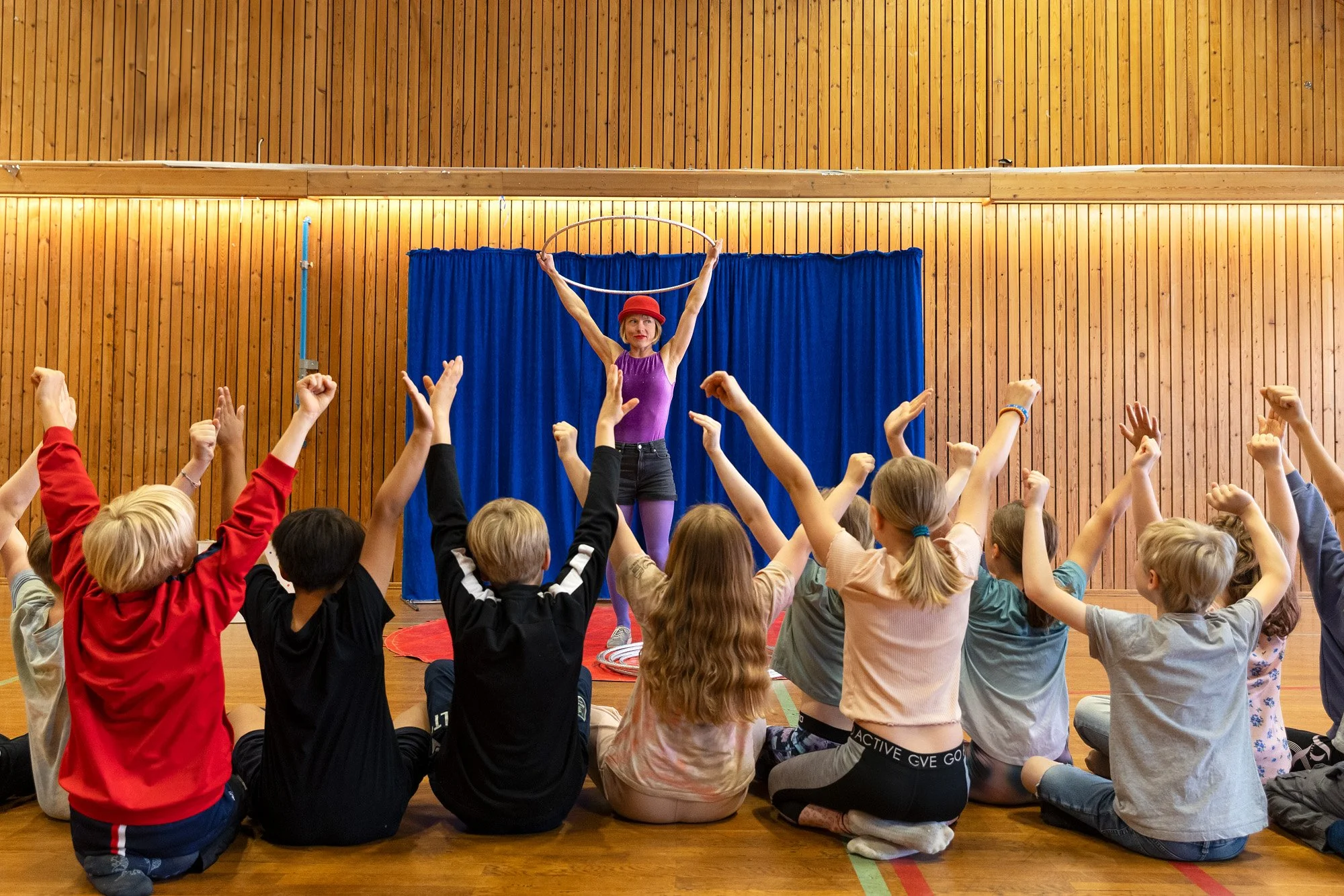Kvinnelig sirkusartist holder en rockering over hodet foran et barnepublikum som strekker armene i lufta