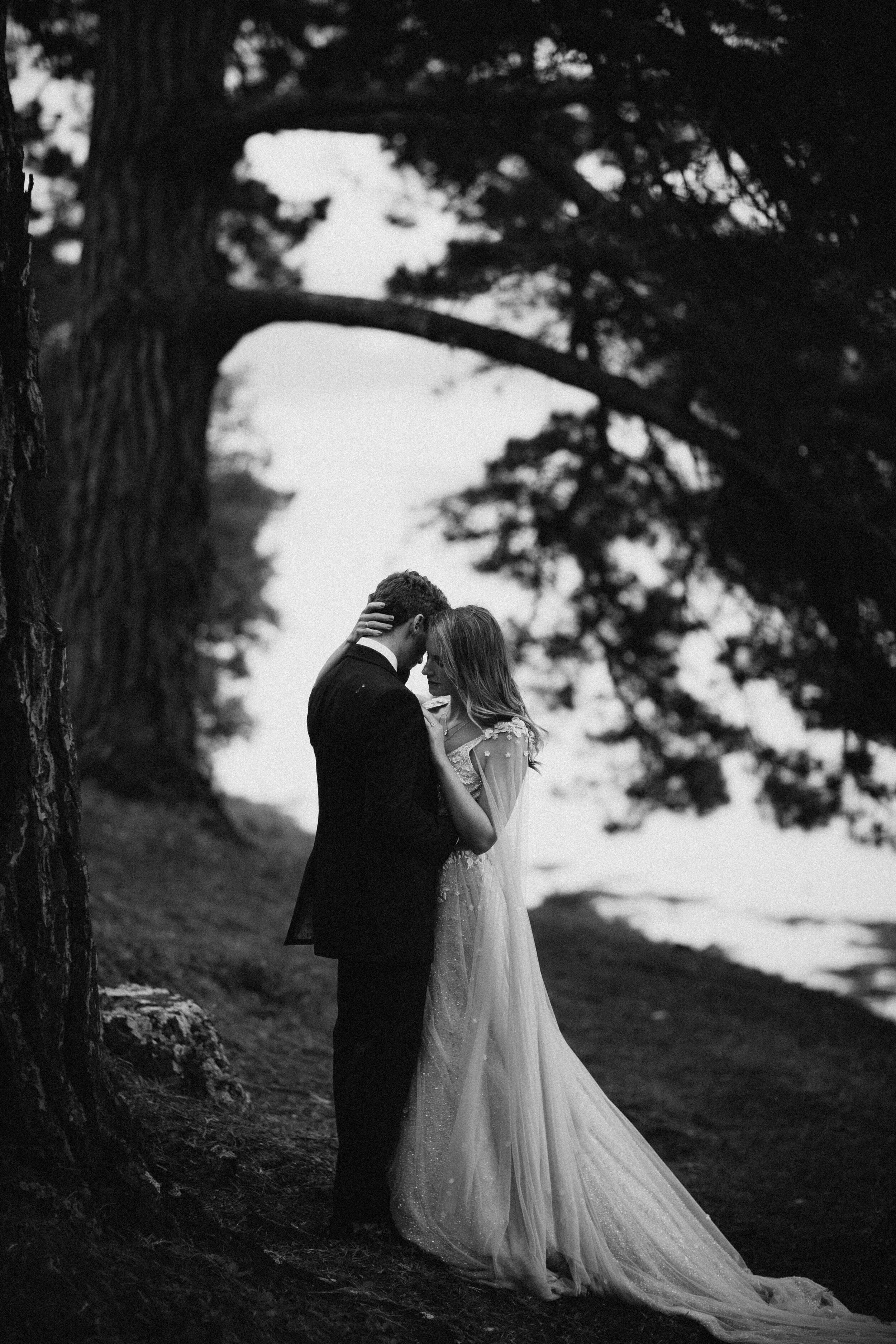 Male model Matt Sharman holds female model Lara wearing a black tuxedo, white shirt and black bow tie in a Cornish forest for Fern Godfrey Weddings